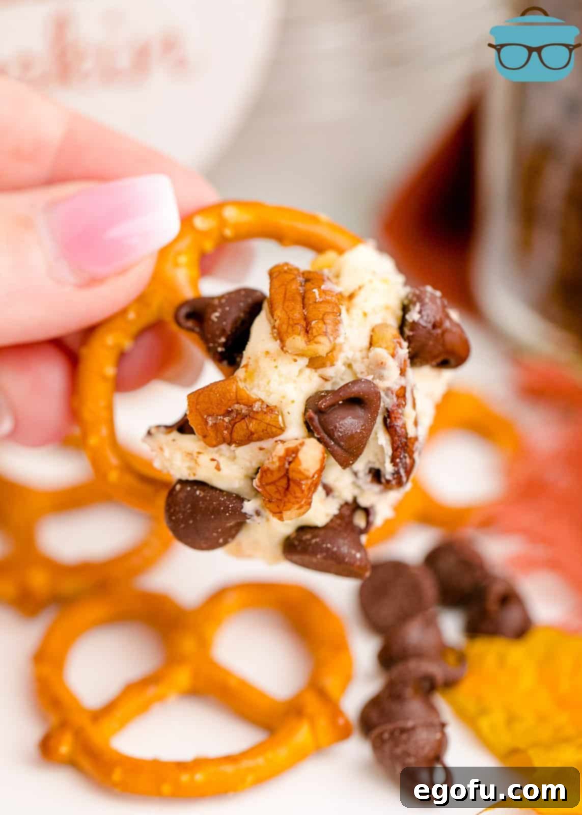A hand holding a pretzel dipped into the rich and creamy Turkey Dessert Cheeseball, illustrating how to enjoy it.