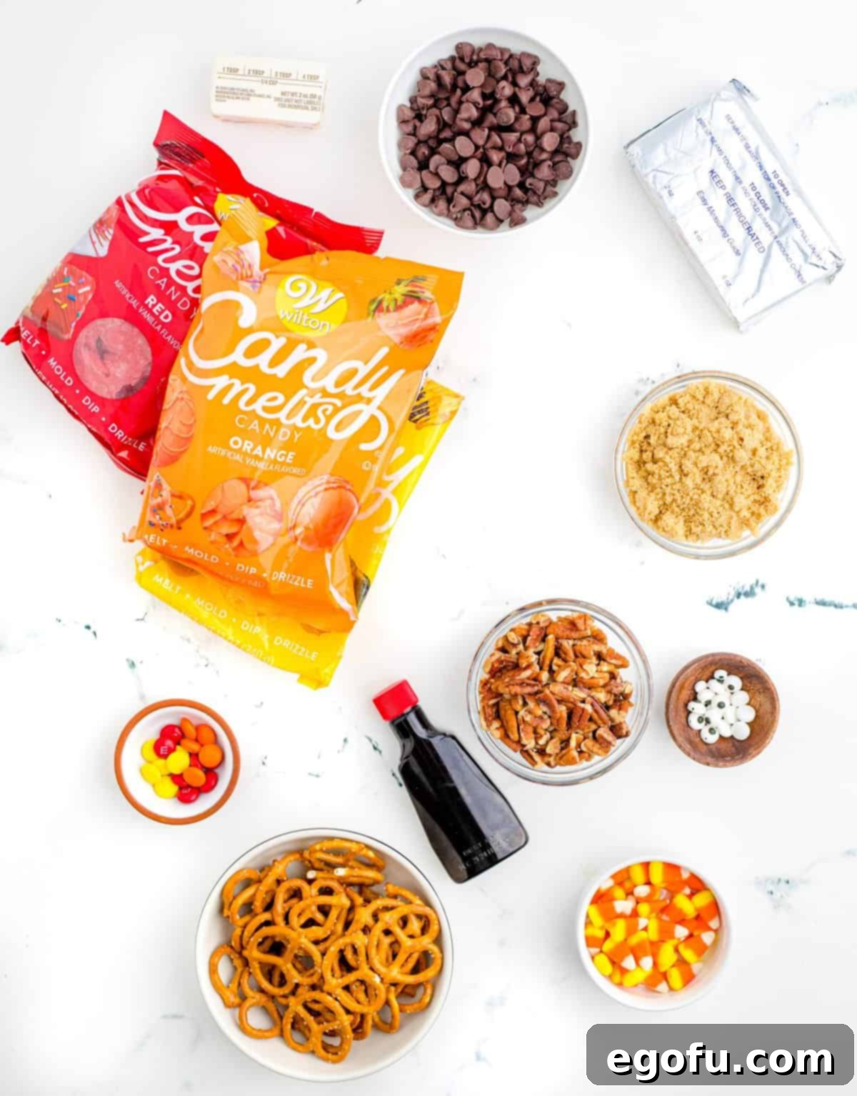 All ingredients for the Turkey Dessert Cheeseball laid out: cream cheese, salted butter, light brown sugar, pecans, semi-sweet chocolate chips, vanilla extract, candy corn, candy eyes, red M&M, and colored candy melts.