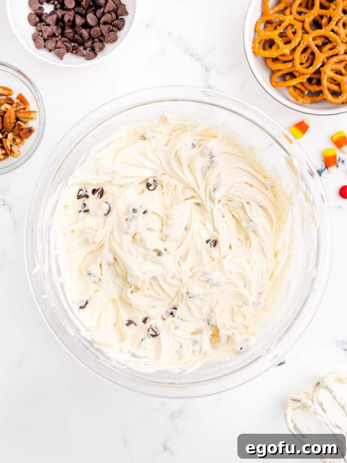 Brown sugar, vanilla extract, chopped pecans, and semi-sweet chocolate chips being mixed into the cream cheese base.