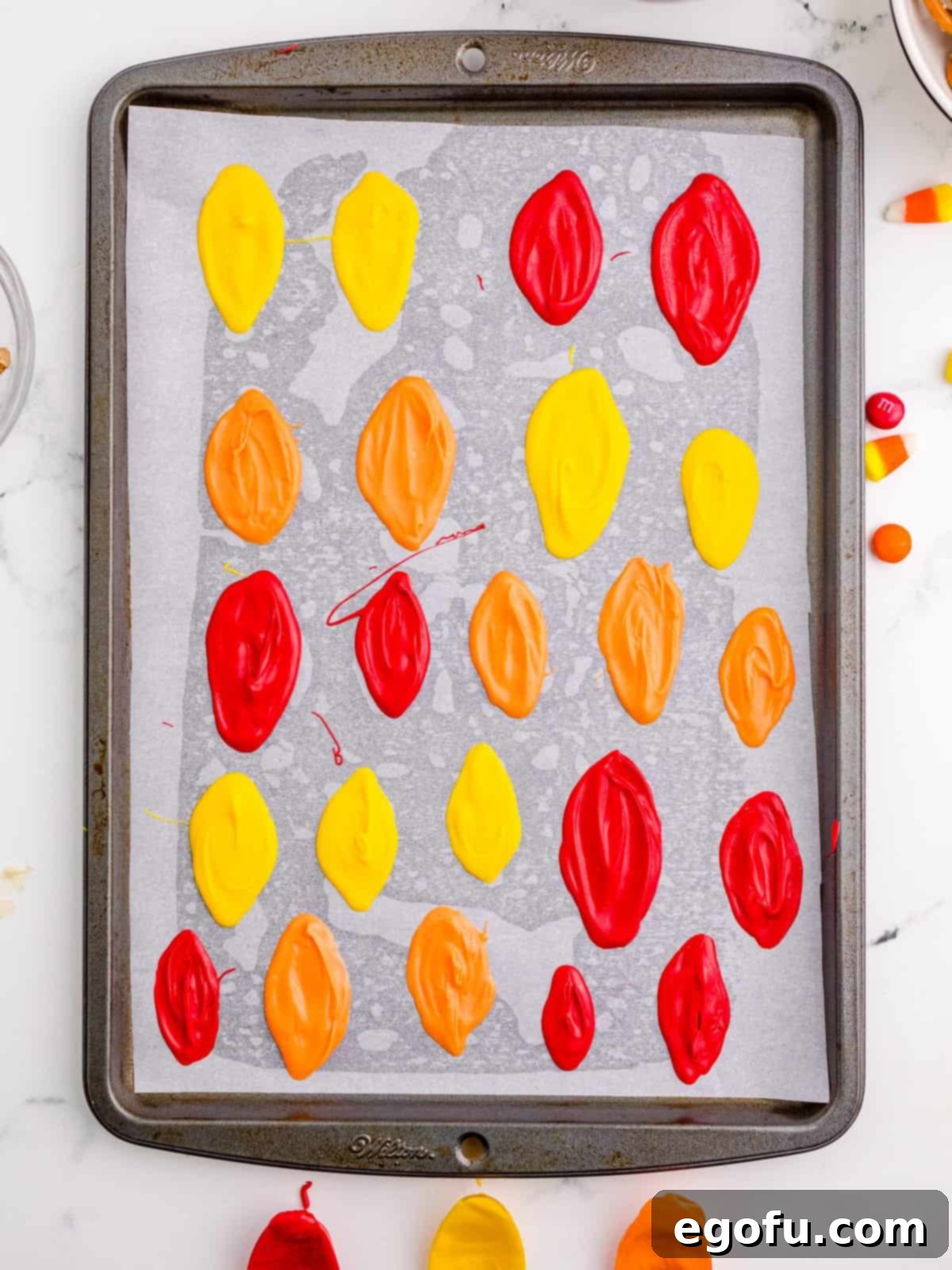 Candy melts spread into various feather shapes on a parchment-lined baking sheet, chilling to harden.