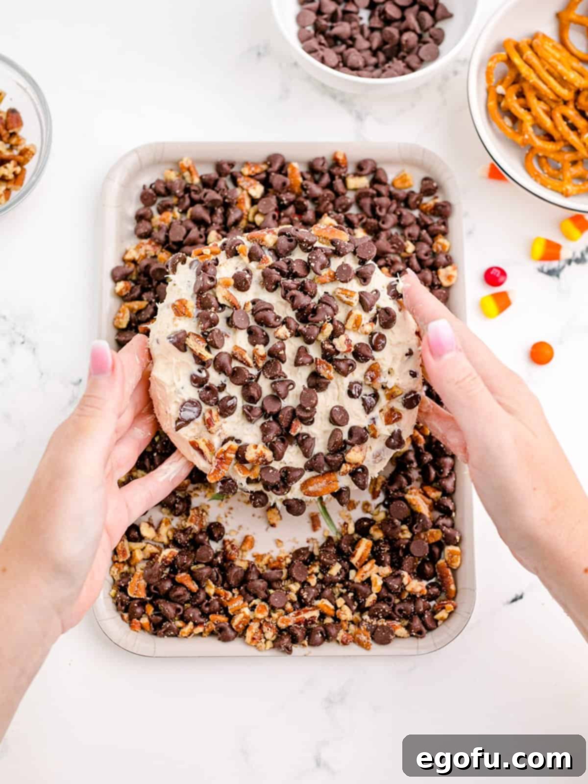 The chilled cheeseball being rolled in a mixture of chopped pecans and semi-sweet chocolate chips for a rich coating.