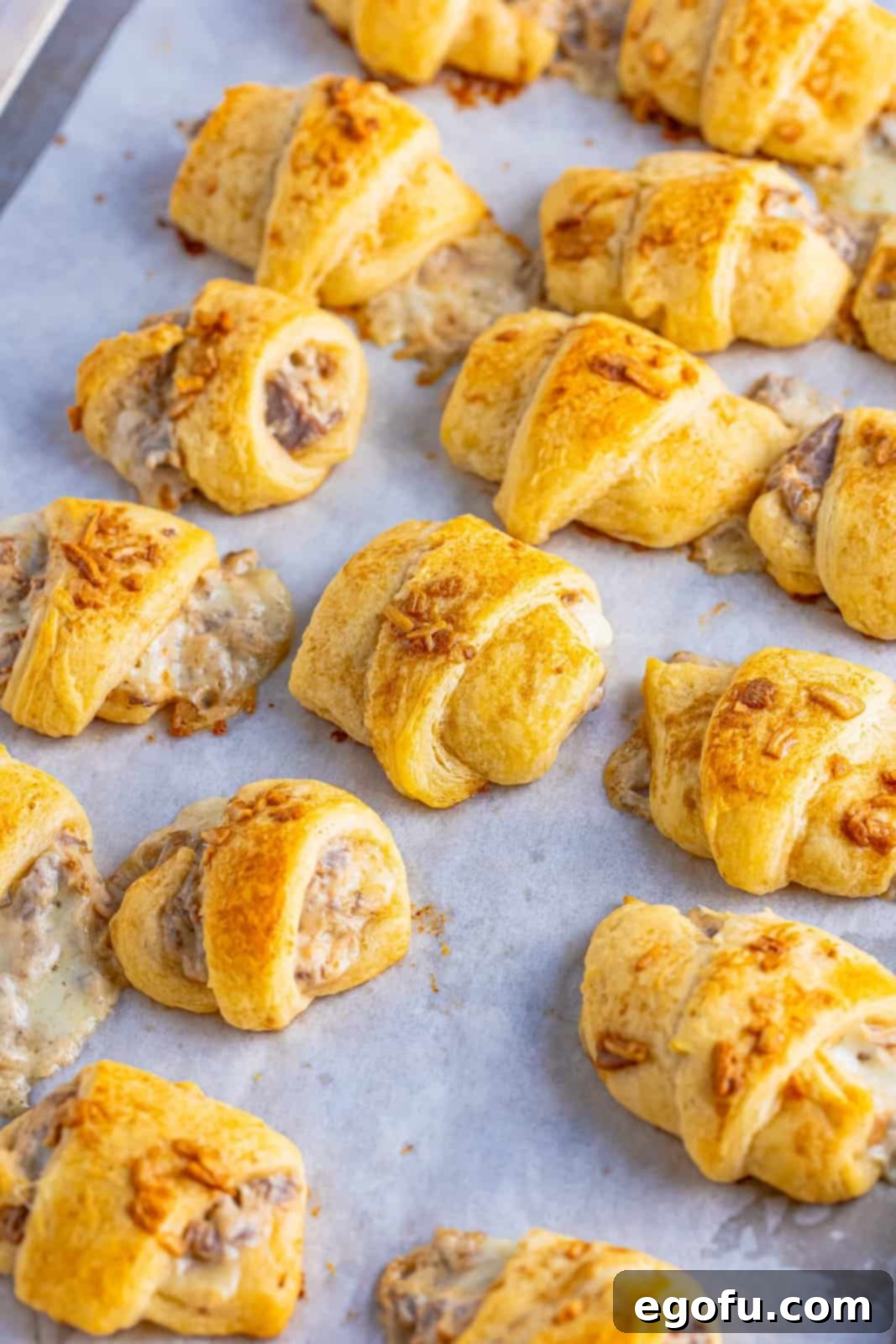 Finished crescent puffs on parchment lined baking sheet.