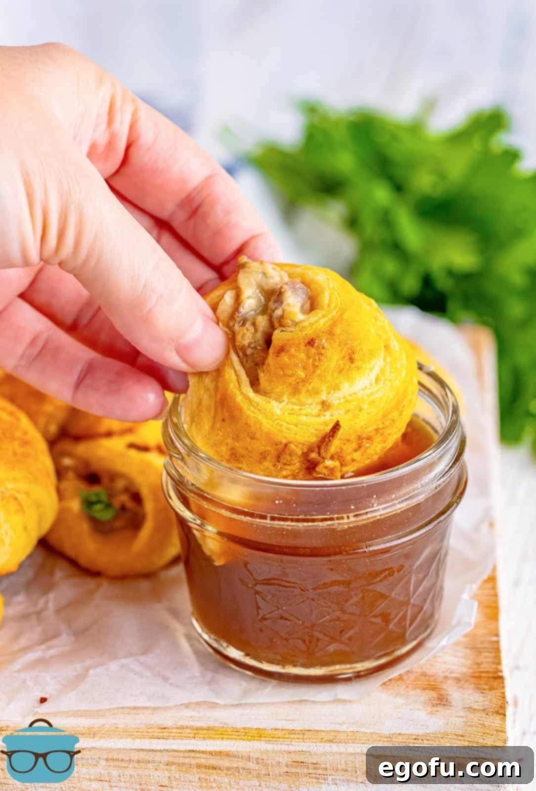 Hand dipping one of the French Dip Crescent Puffs into the au jus.