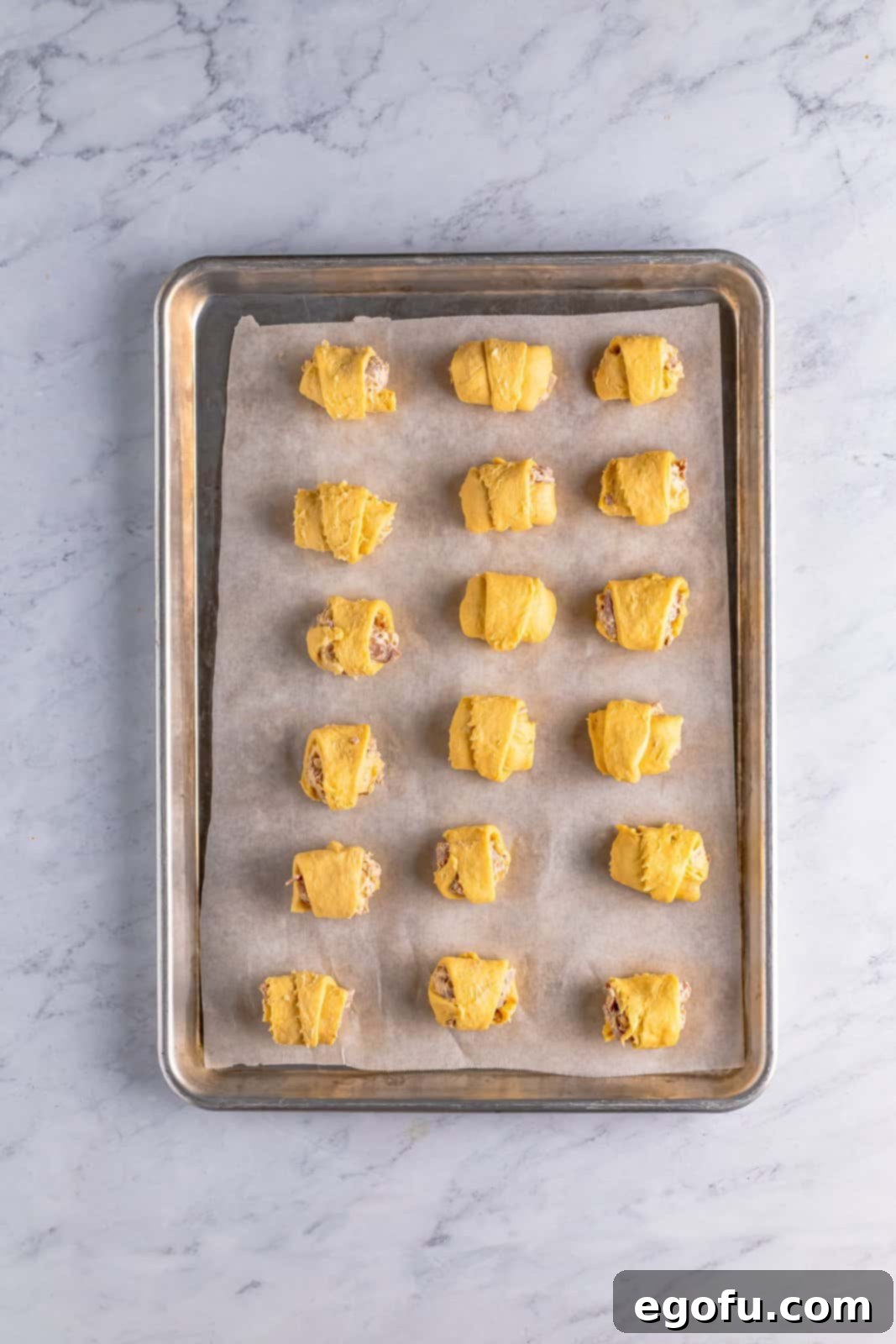 Rolled up crescent puffs on parchment lined baking sheet.