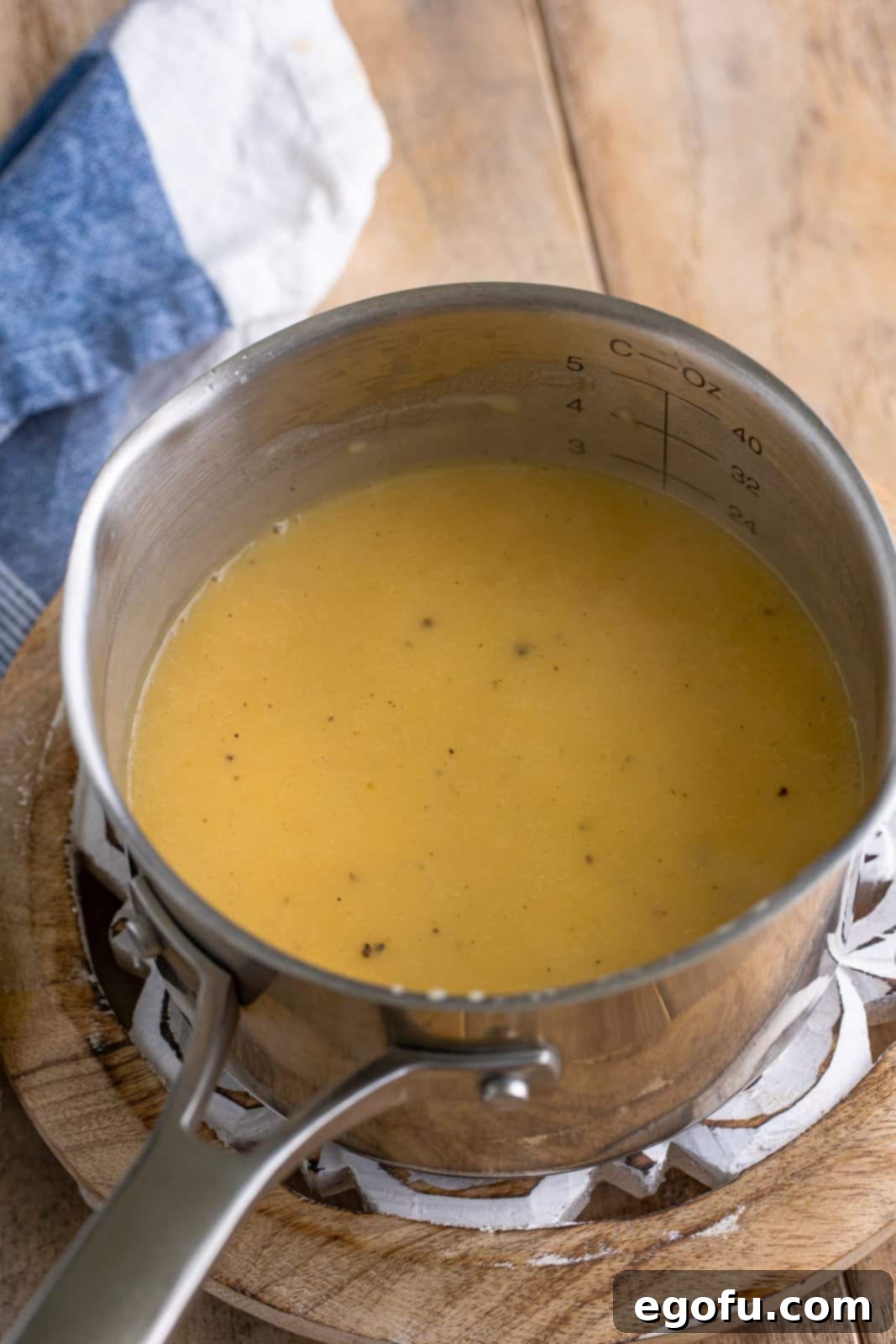 The combined turkey drippings and chicken stock mixture being steadily added to the butter and flour roux, transforming into a rich, simmering gravy.