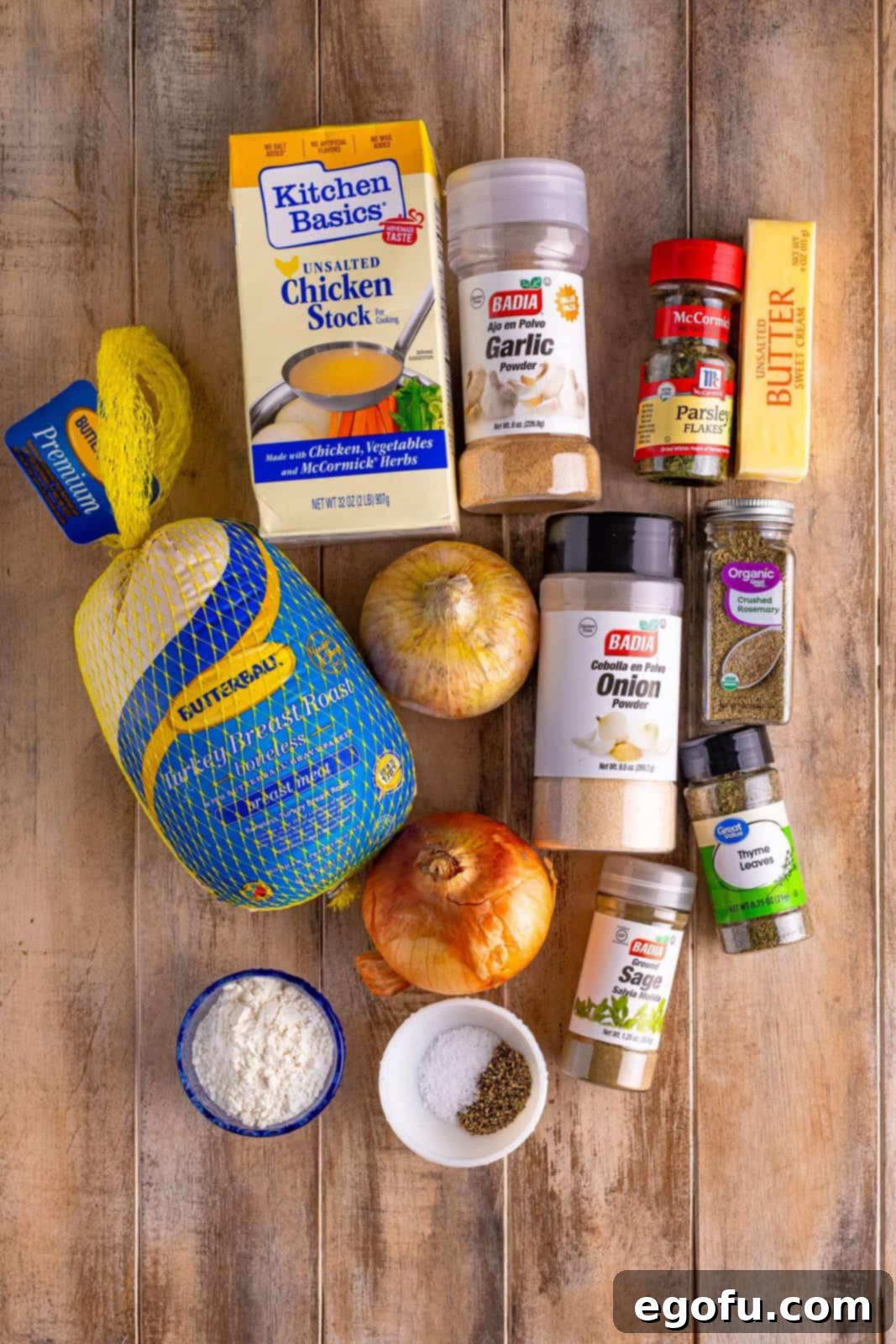 A comprehensive flat lay image showcasing all the ingredients required for preparing a Slow Cooker Turkey Breast, including fresh onions, boneless turkey breast, unsalted butter, a variety of dried herbs and spices, chicken stock, and all-purpose flour.