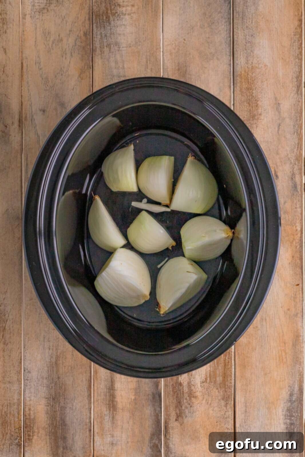 Onion wedges meticulously placed in the bottom of a crock pot, forming a natural trivet and flavorful base for the turkey breast.