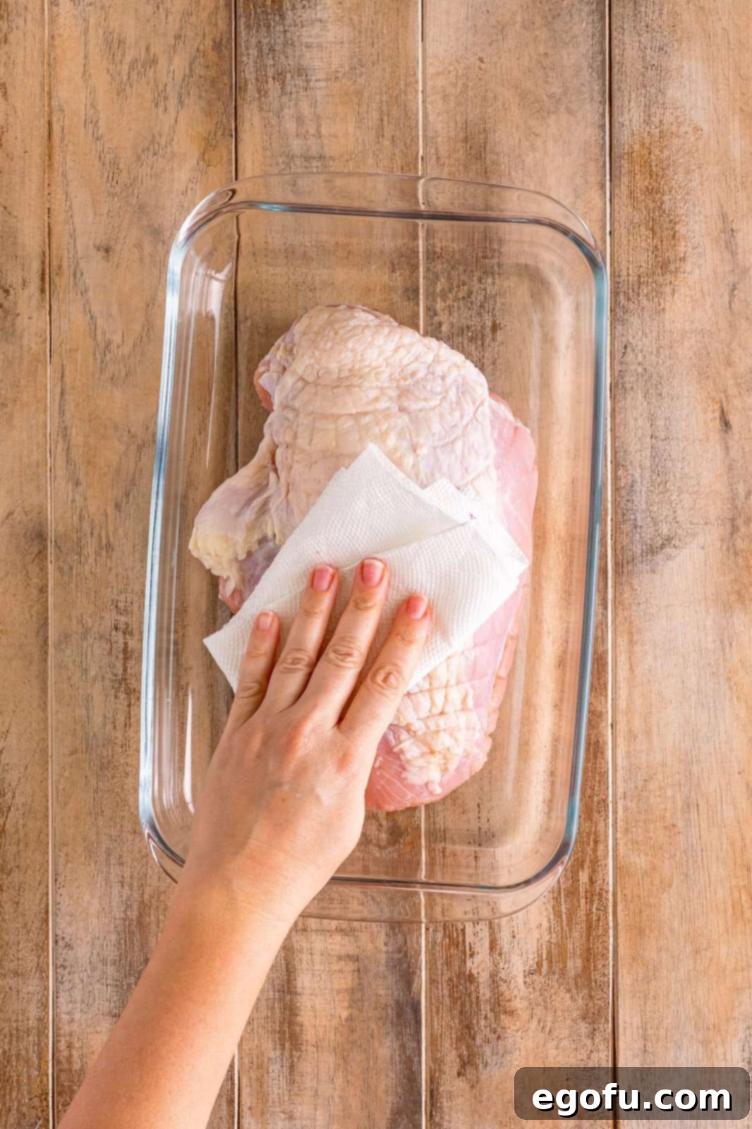 A hand gently patting a boneless turkey breast dry with paper towels, preparing its surface for the herb butter rub.