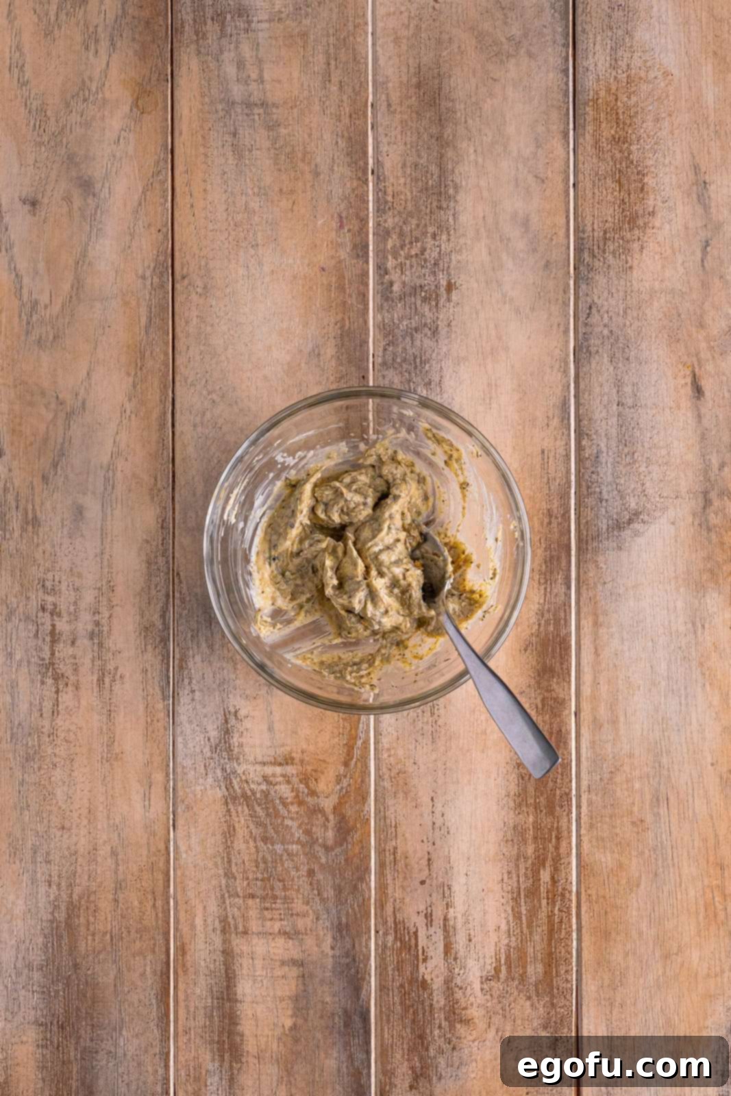 A small bowl holding the thoroughly mixed herb butter rub, showcasing its rich texture and aromatic blend of spices.