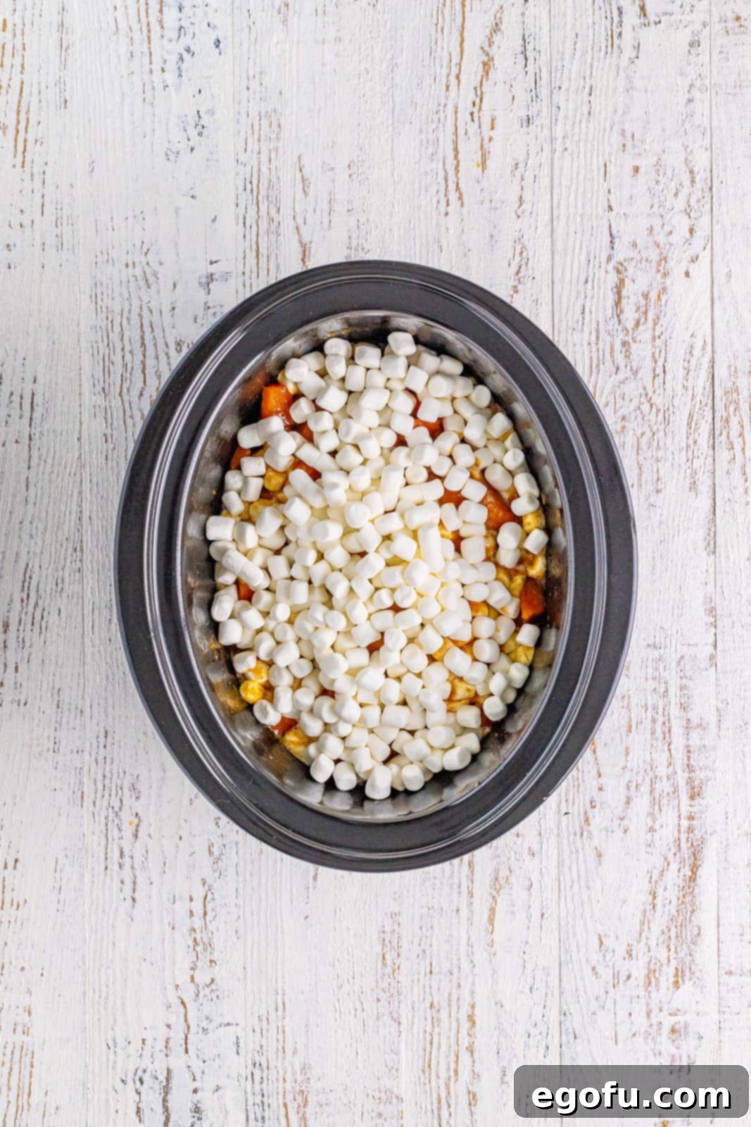 Marshmallows added to the top of the sweet potato mixture in the crock pot, forming a white layer.