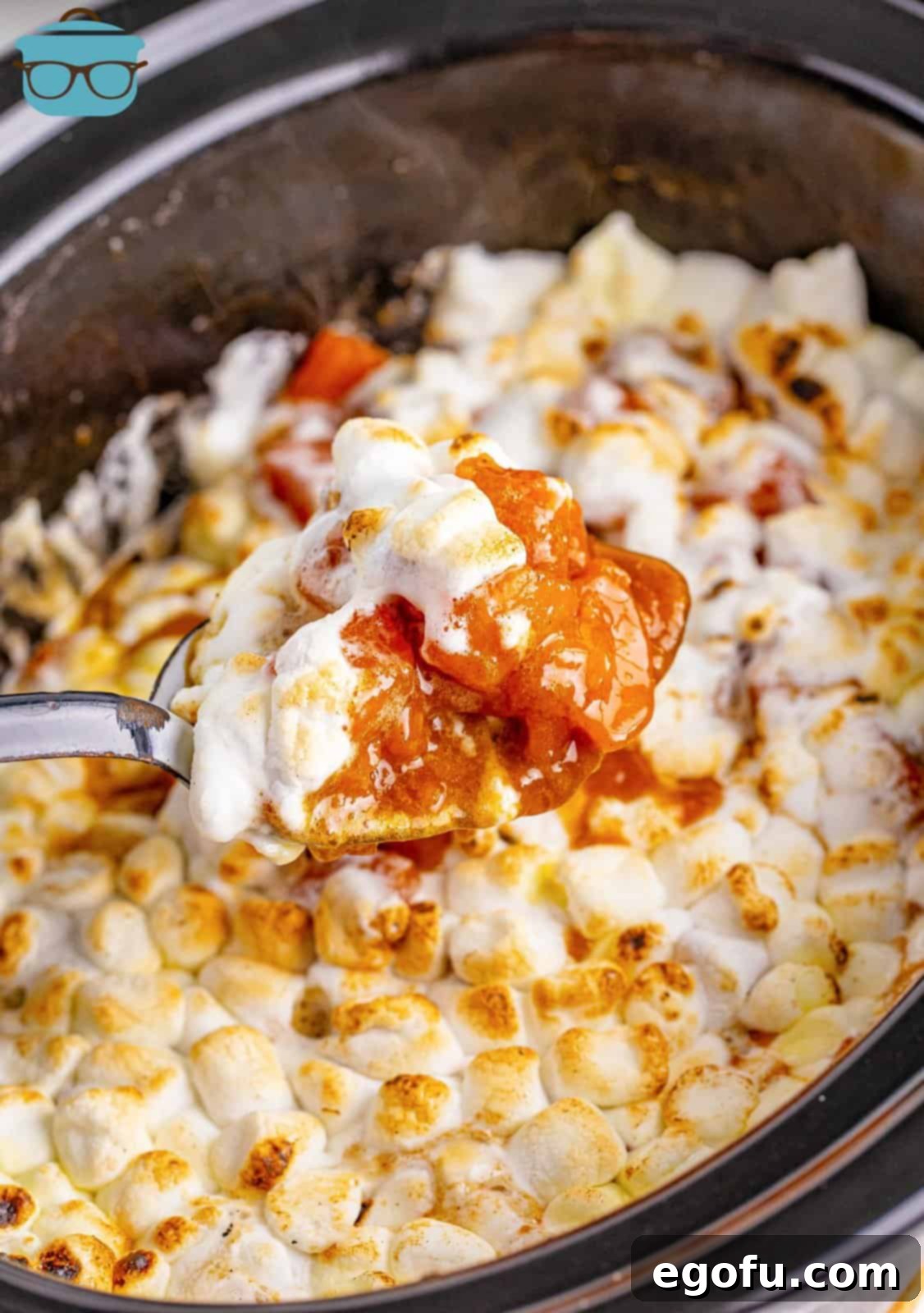 A serving spoon holding up some of the Crock Pot Candied Yams Casserole out of crock pot, displaying the melted marshmallows and tender sweet potatoes.