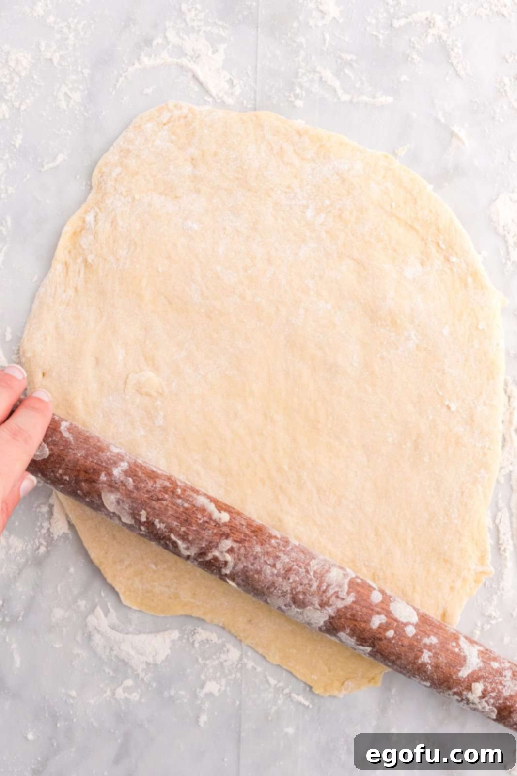 Dough being meticulously rolled out into a perfect circle on a lightly floured surface.
