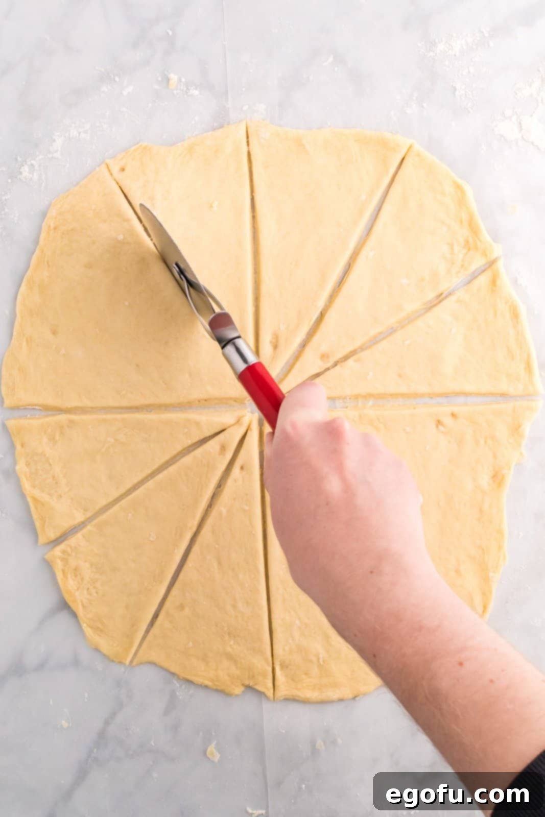 A pizza cutter being used to divide the circular dough into 12 perfectly equal triangles.