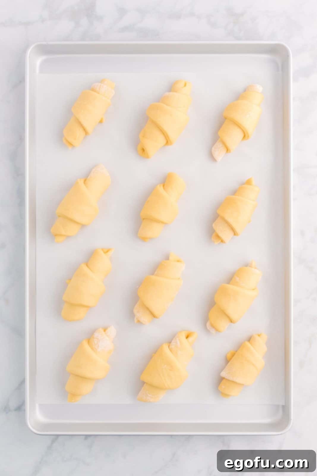 Shaped crescent roll dough carefully placed onto a parchment-lined baking sheet, with the point side down.