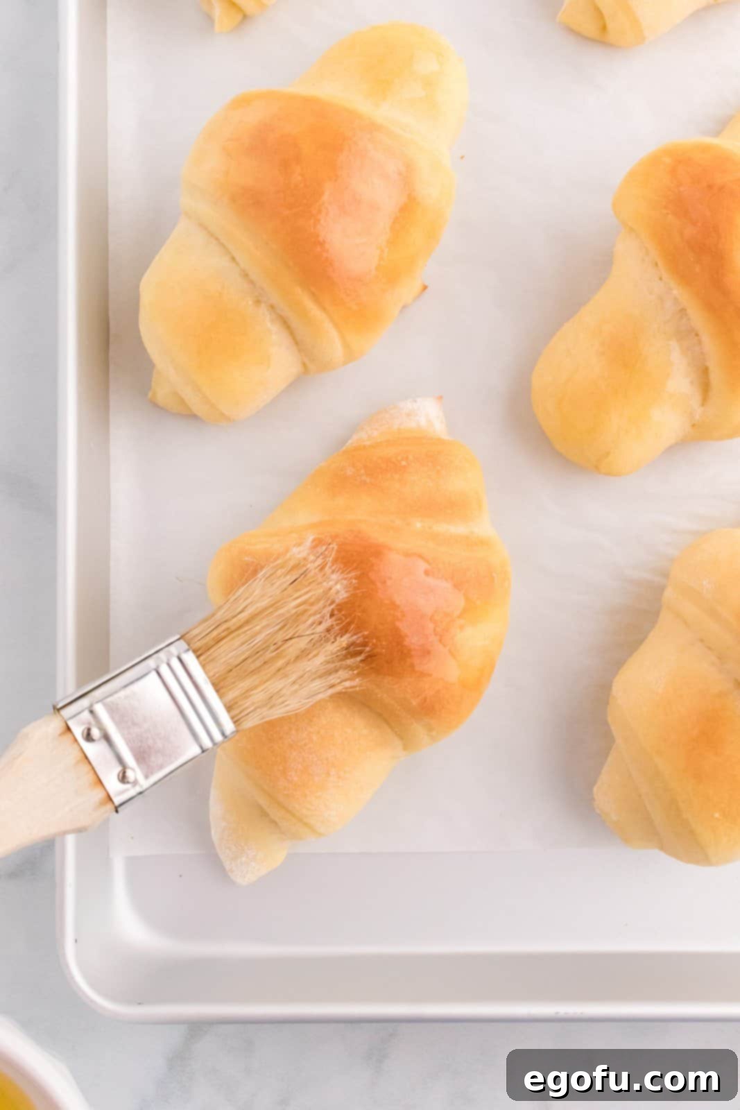 Freshly baked crescent rolls being brushed with melted butter for a final touch of richness and shine.