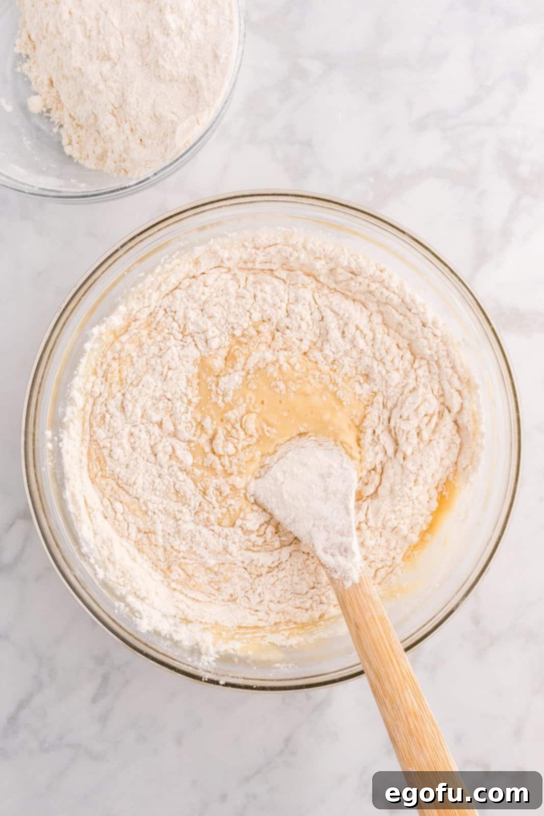 All-purpose flour being slowly added to the butter and yeast mixture in a large mixing bowl.