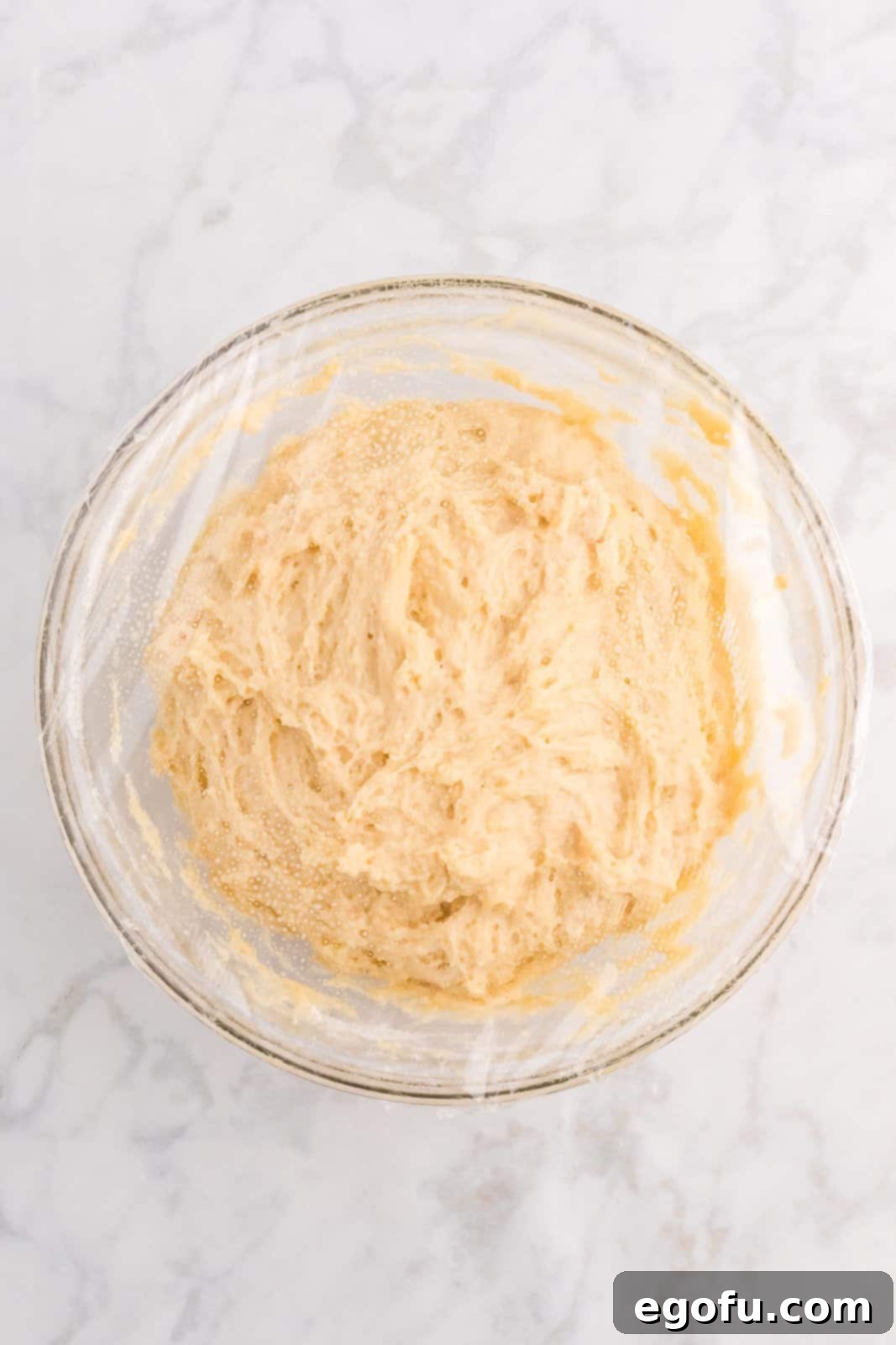 A bowl of dough covered with plastic wrap, sprayed with cooking spray, ready for refrigeration.