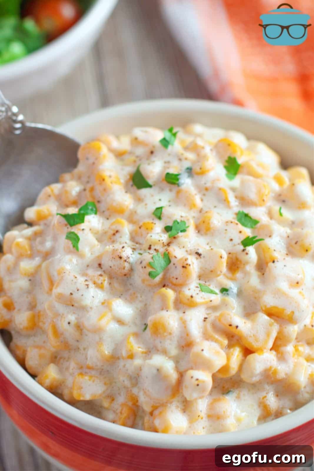 Crock Pot Creamed Corn in bowl with spoon, topped with parsley.