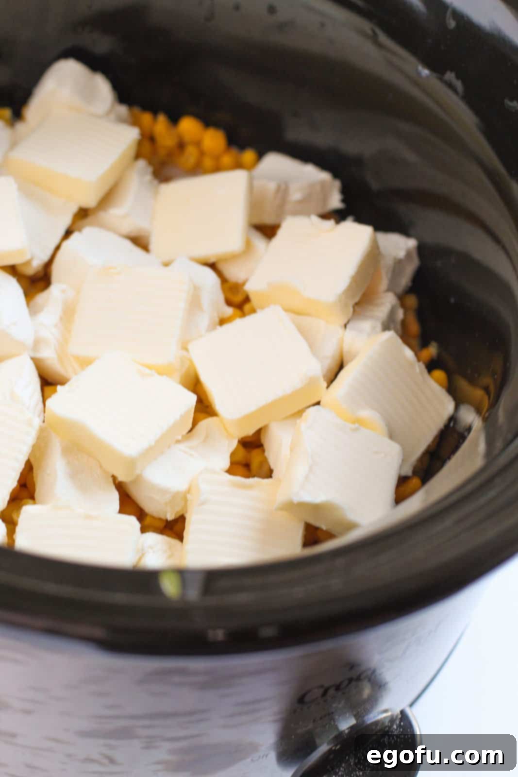 Cubed cream cheese and butter added to the top of corn.
