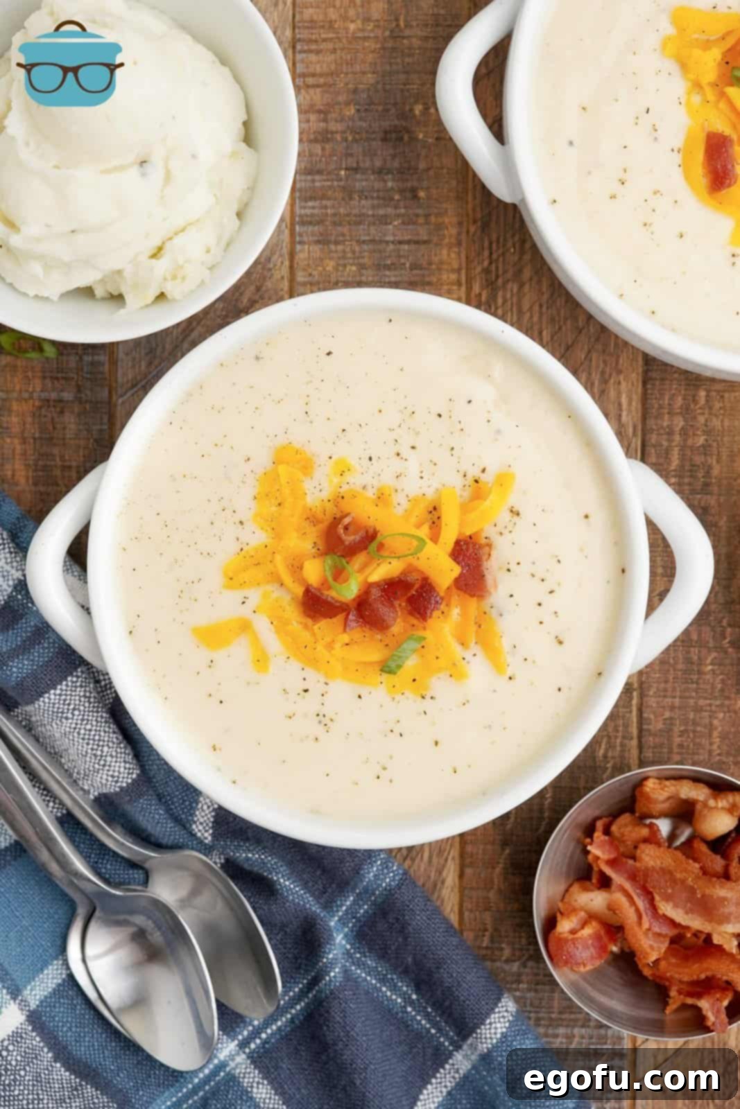 Overhead photo of Mashed Potato Soup in handled bowl topped with cheese, bacon and green onions.