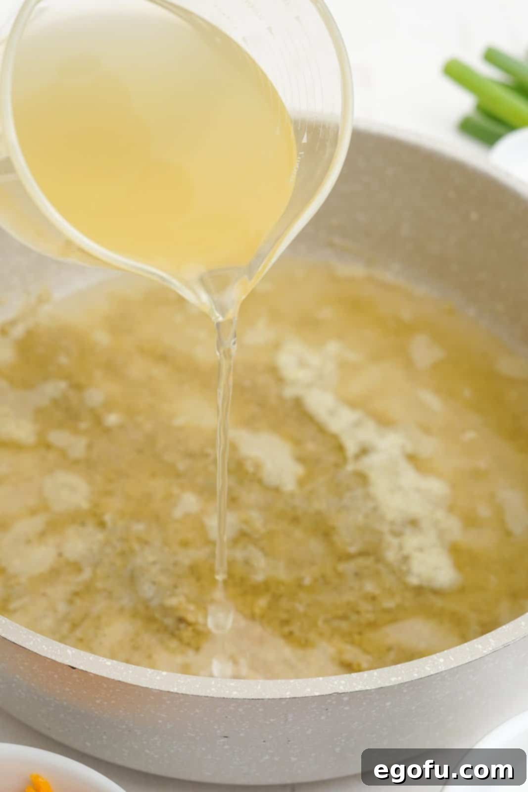 Chicken broth being slowly poured into the roux while being whisked in a pot.