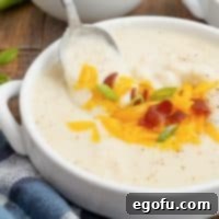 Close up photo of Mashed Potato Soup in bowl with garnishes with spoon slightly pulling out of bowl.