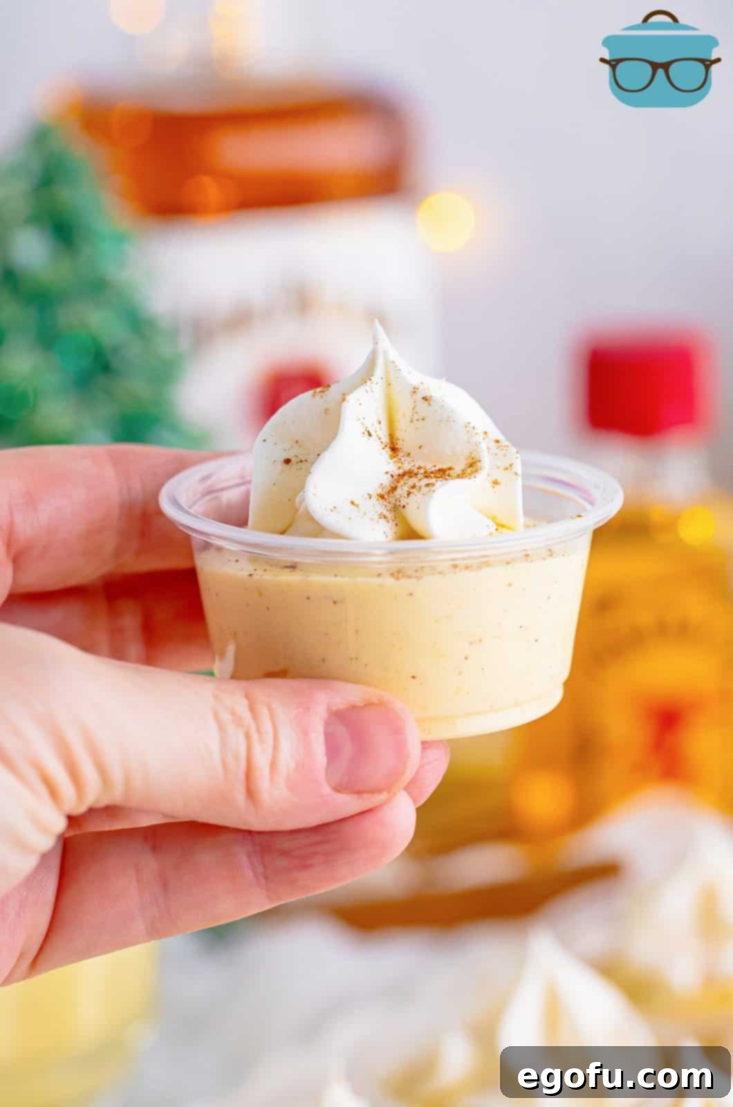Hand holding up one of the Egg Nog Pudding Shots, showing its creamy texture and festive garnish.