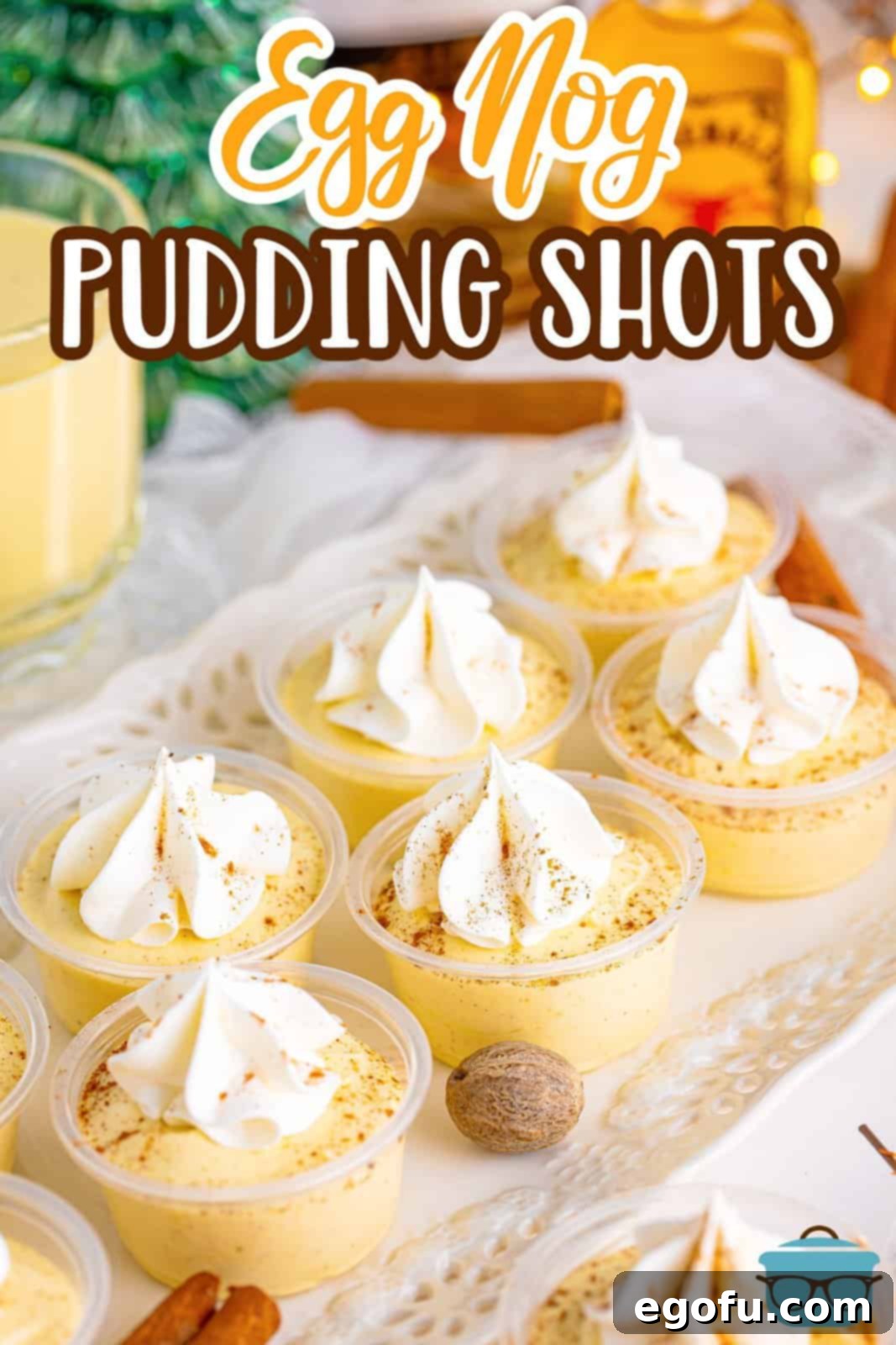 Slightly overhead Pinterest image of Egg Nog Pudding Shots on white platter, garnished with nutmeg and cinnamon sticks on platter.