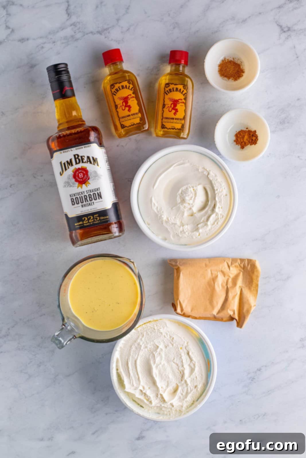 Ingredients needed: instant vanilla pudding mix, eggnog, bourbon, fireball cinnamon whiskey, ground cinnamon, ground nutmeg and whipped topping arranged for Eggnog Pudding Shots.