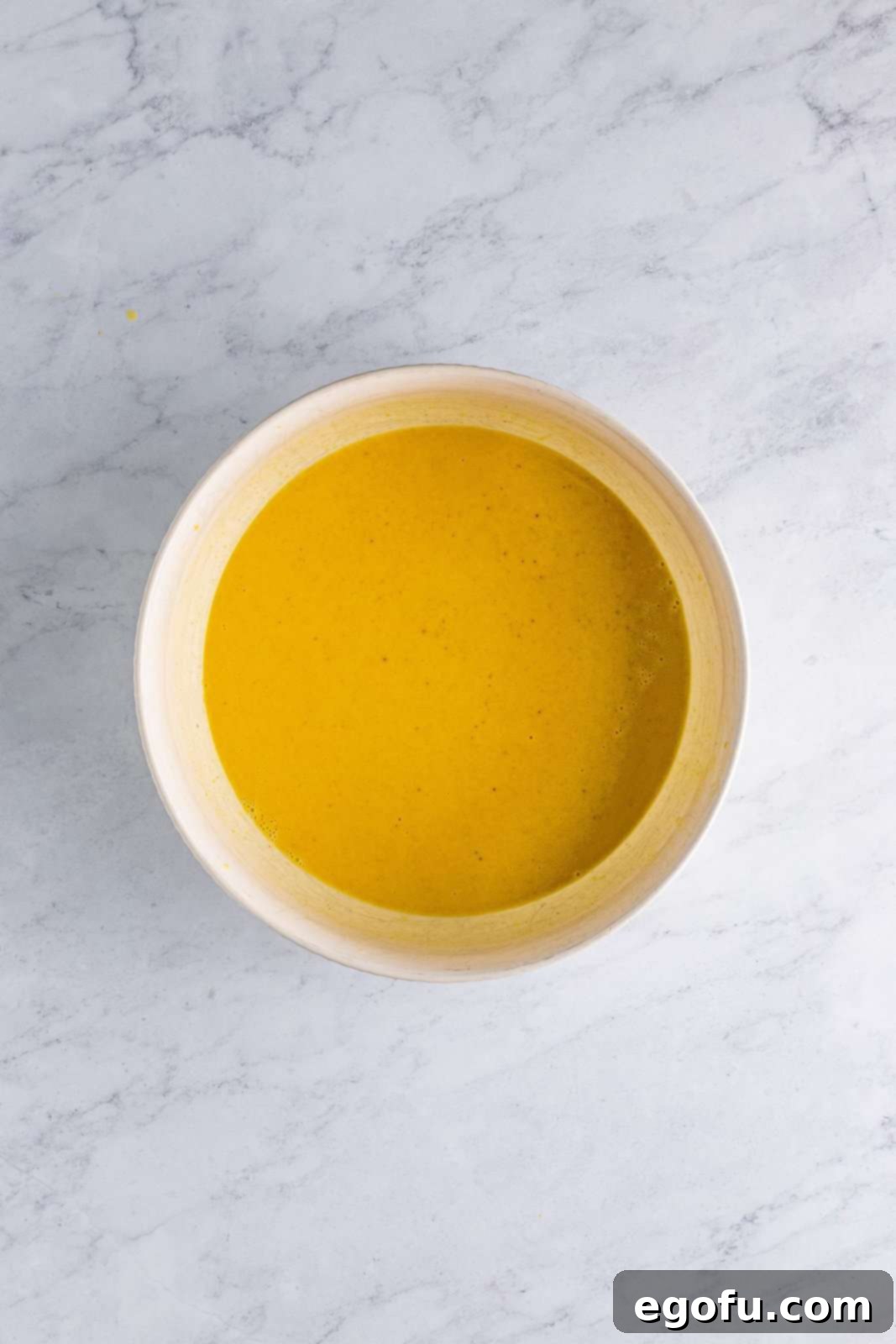 Pudding mix, eggnog, bourbon, cinnamon, and nutmeg whisked together in bowl, showing the initial thickening process.