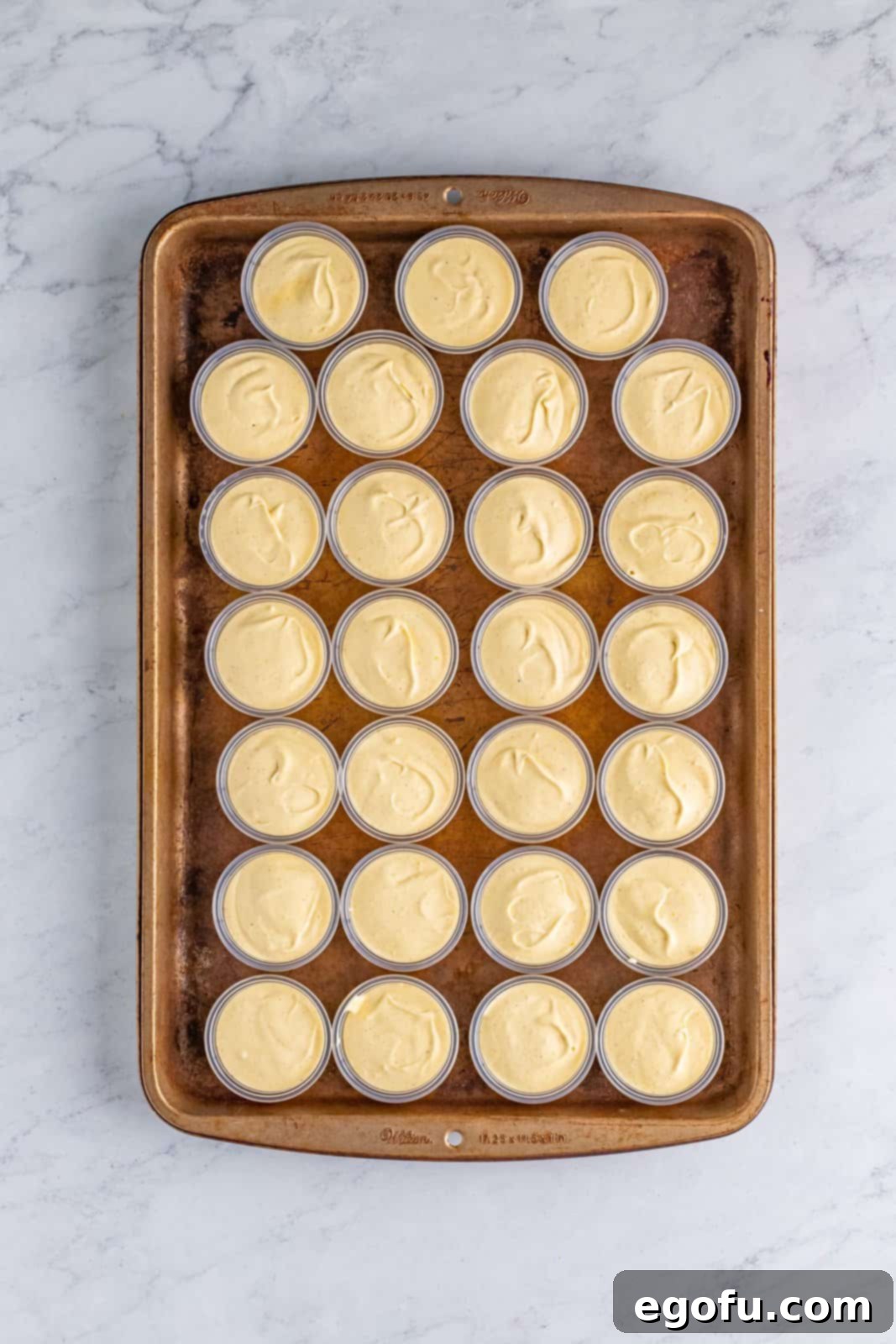 Pudding mixture accurately added to plastic cups on sheet tray, ready for chilling.
