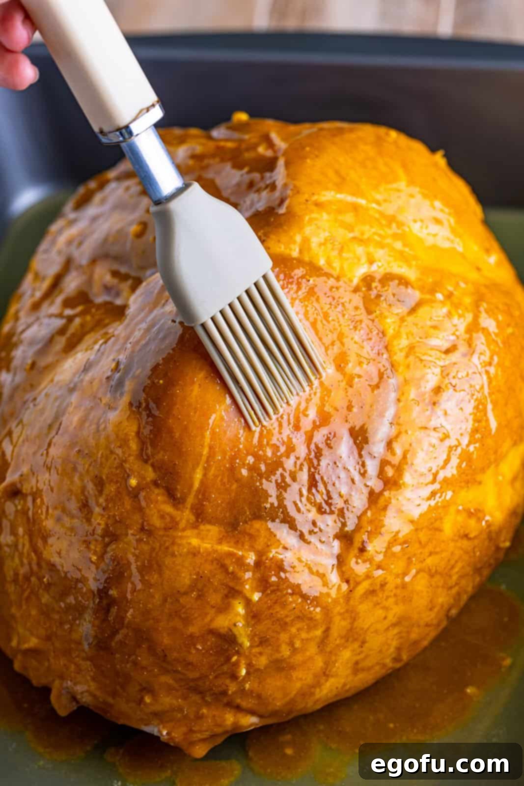Mahogany Glazed Ham 10 A pastry brush applying the first layer of brown sugar glaze over the ham in the roasting pan.