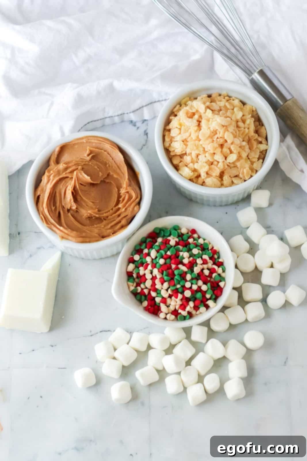 Ingredients needed for Crock Pot Avalanche Cookies: almond bark, creamy peanut butter, Rice Krispies cereal, mini marshmallows, and holiday mini chips or sprinkles, laid out on a kitchen counter.