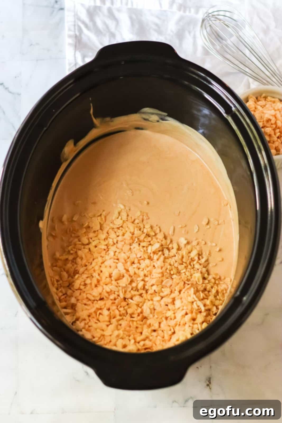 Melted almond bark and peanut butter in crock pot with Rice Krispies cereal added and partially mixed.