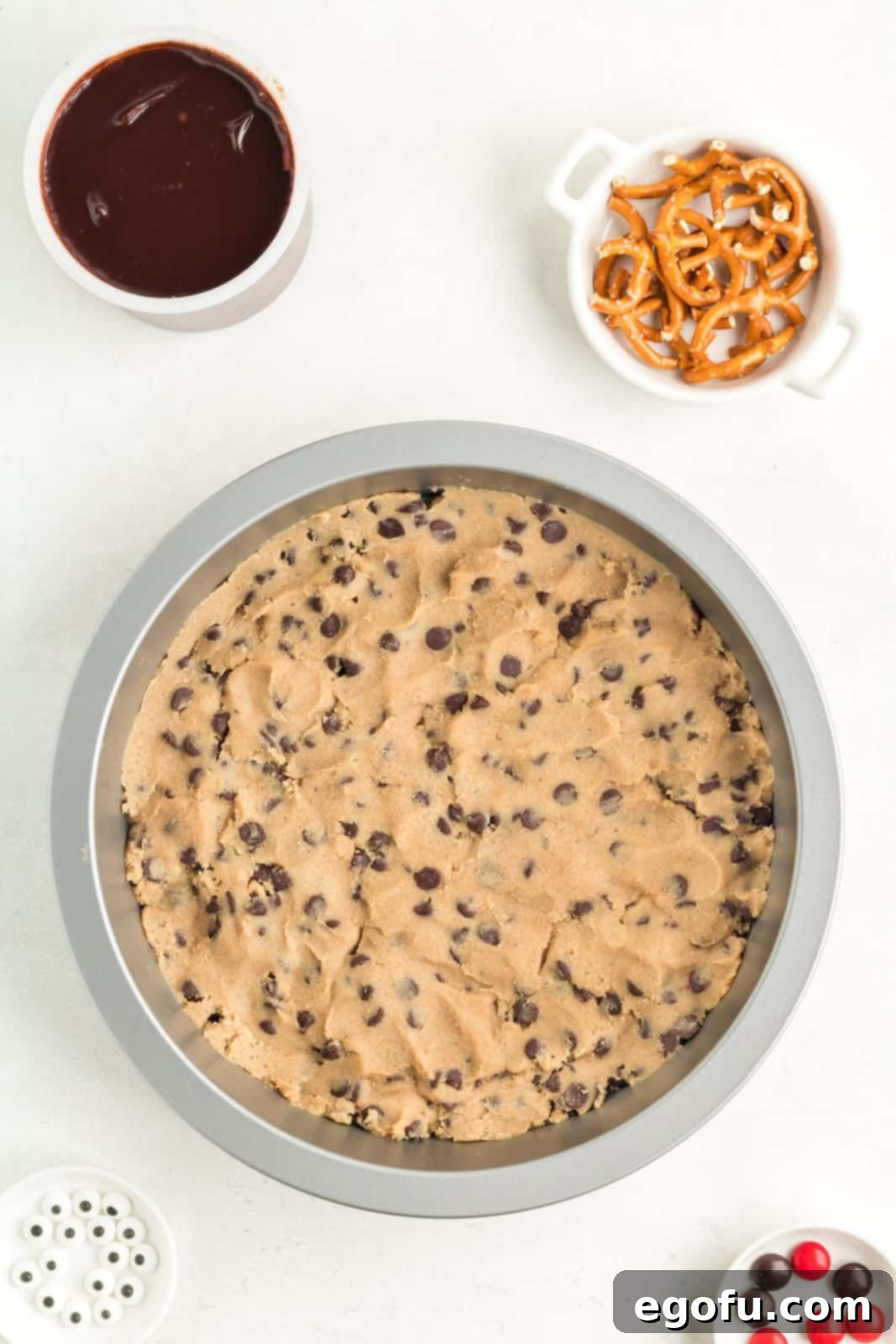 Chocolate chip cookie dough expertly pressed into a round baking pan, creating an even layer and ready to be baked into the base of the cookie bars.
