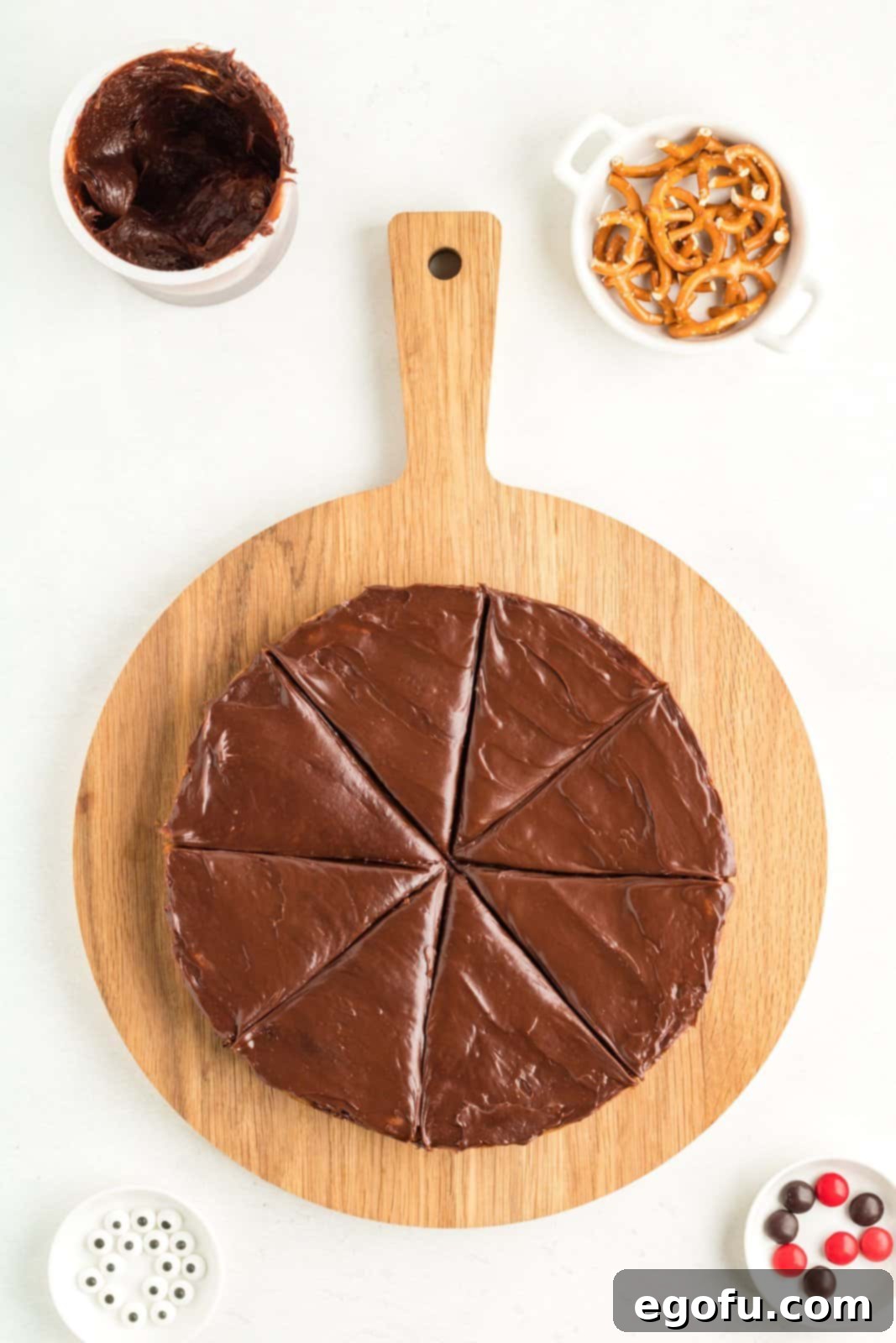 A large round cookie bar, uniformly frosted with chocolate and neatly cut into 8 pizza-like slices, positioned on a round cutting board, ready for the reindeer decorations.