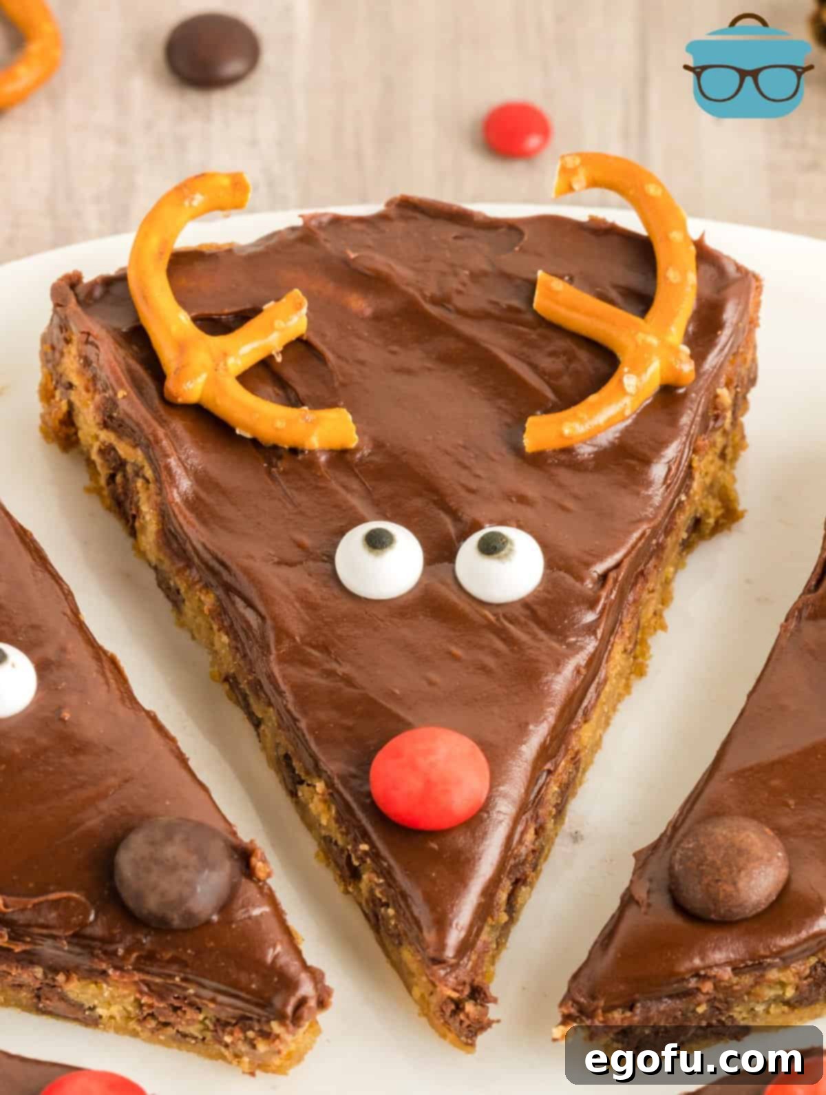 A close-up view of a single, perfectly decorated Reindeer Cookie Bar, showcasing the intricate details of its pretzel antlers, M&M nose, and candy eyes, artfully placed on a white platter.