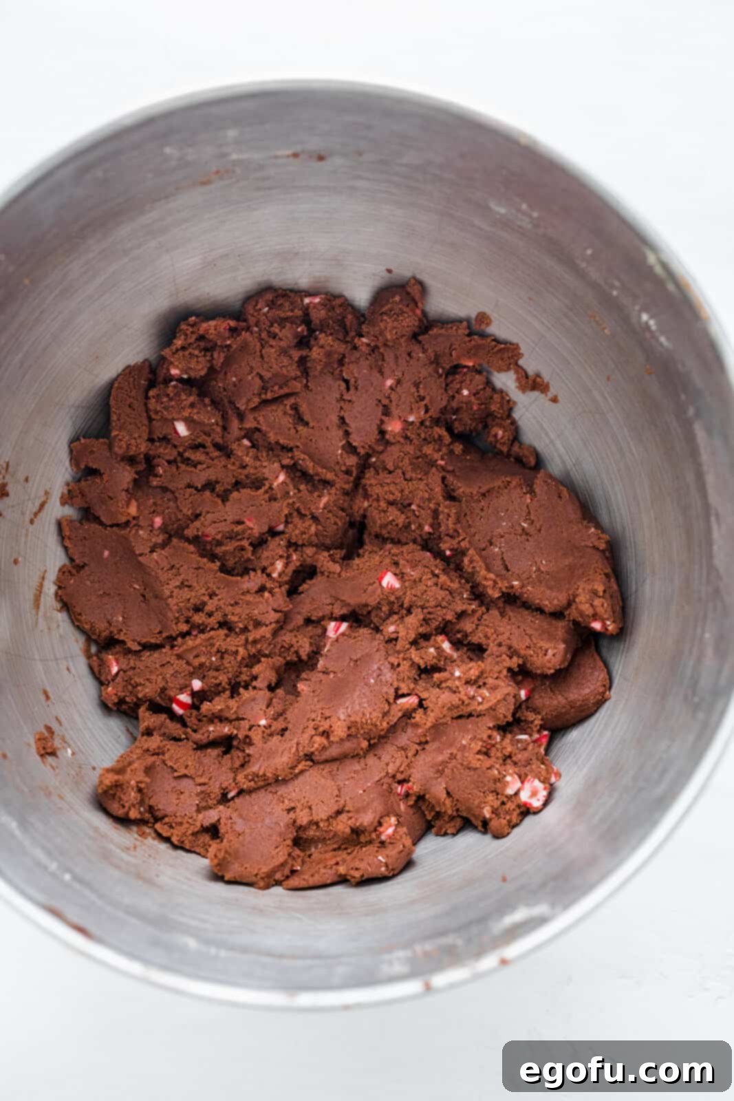 Finished dough with crushed candy canes folded in in bowl of stand mixer.
