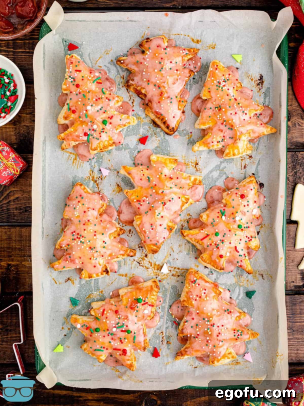Sparkling Spruce Pop Tarts 2 Finished Christmas Tree Pop Tarts on parchment lined pan, glistening with icing and sprinkles.