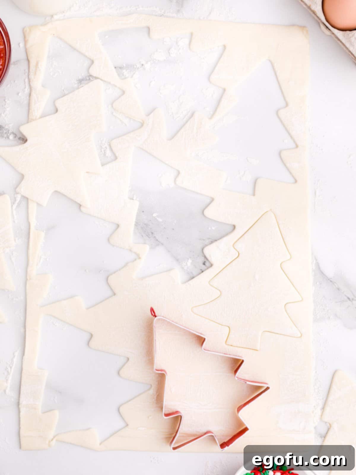 Sparkling Spruce Pop Tarts 5 Christmas tree shapes being cut out of puff pastry using a cookie cutter on a lightly floured surface.