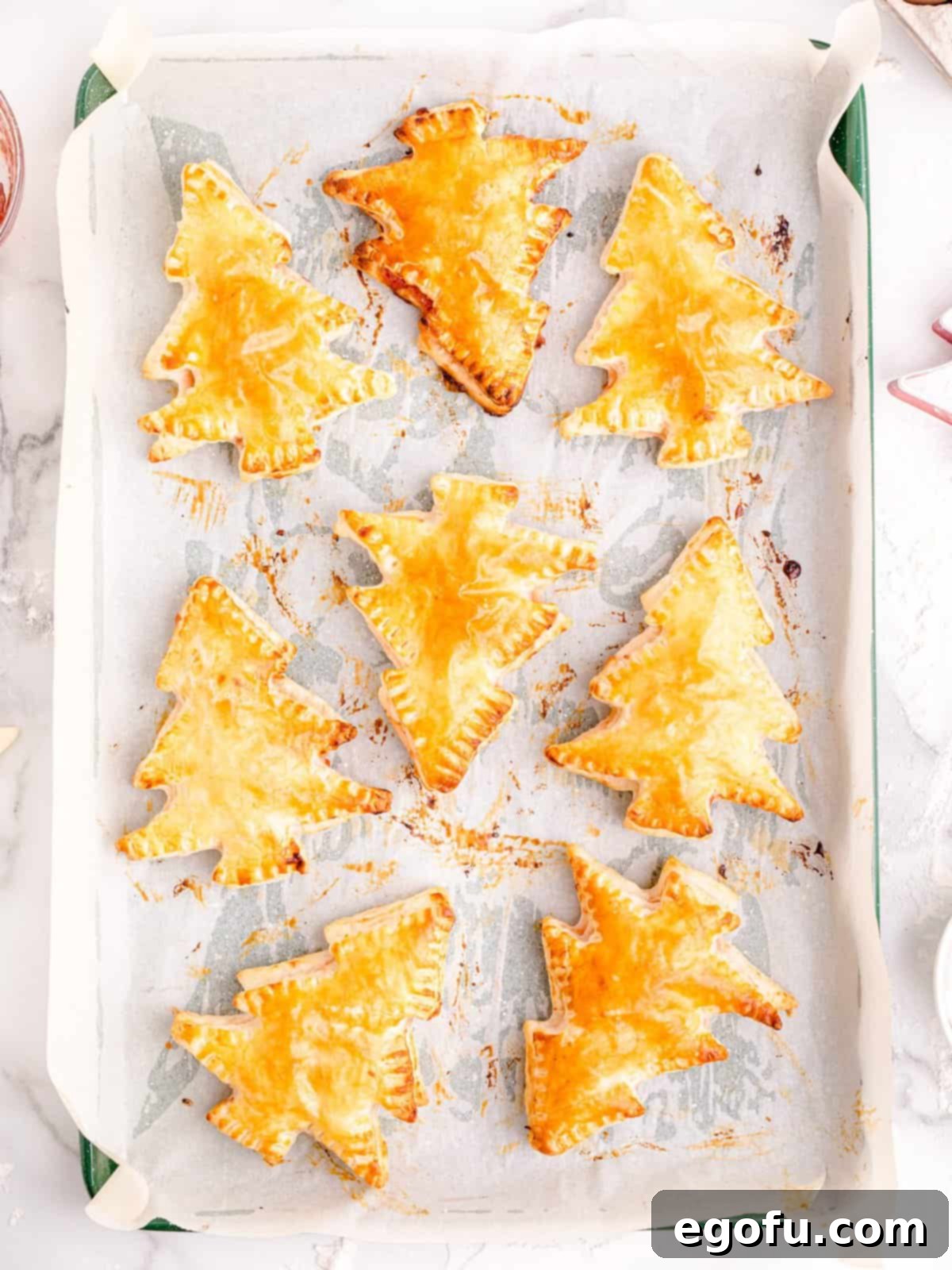 Sparkling Spruce Pop Tarts 8 Freshly baked Christmas Tree Pop Tarts cooling on a parchment-lined baking sheet after being removed from the oven.