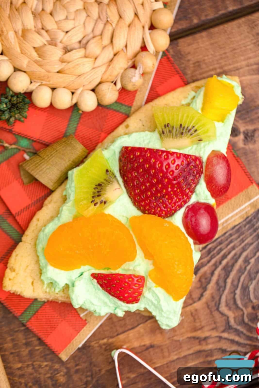A perfectly cut slice of the Christmas Tree Fruit Pizza resting on a festive holiday napkin, ready to be enjoyed.