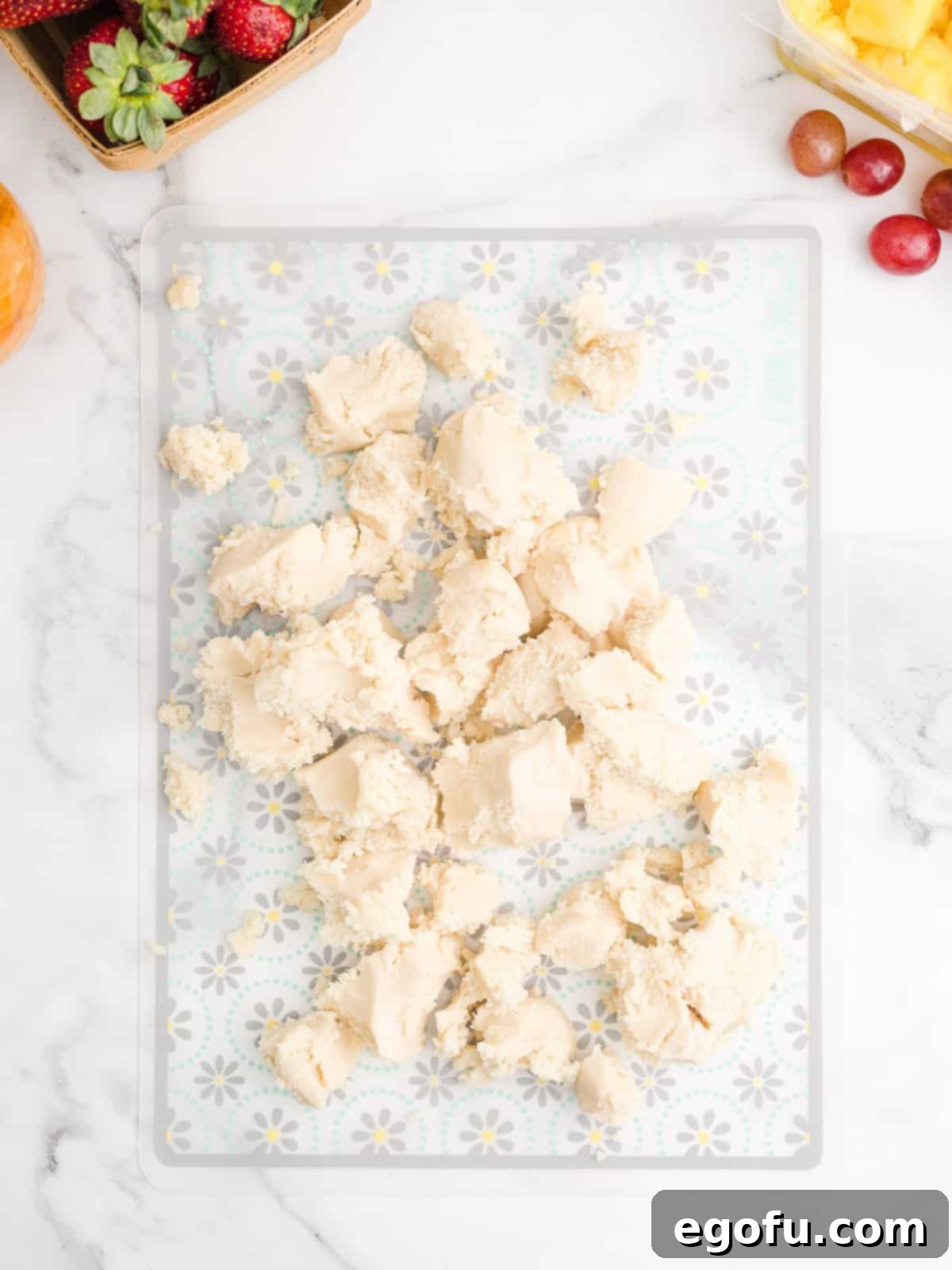 Sugar cookie dough broken up into pieces, ready to be formed into a ball, on a baking mat.