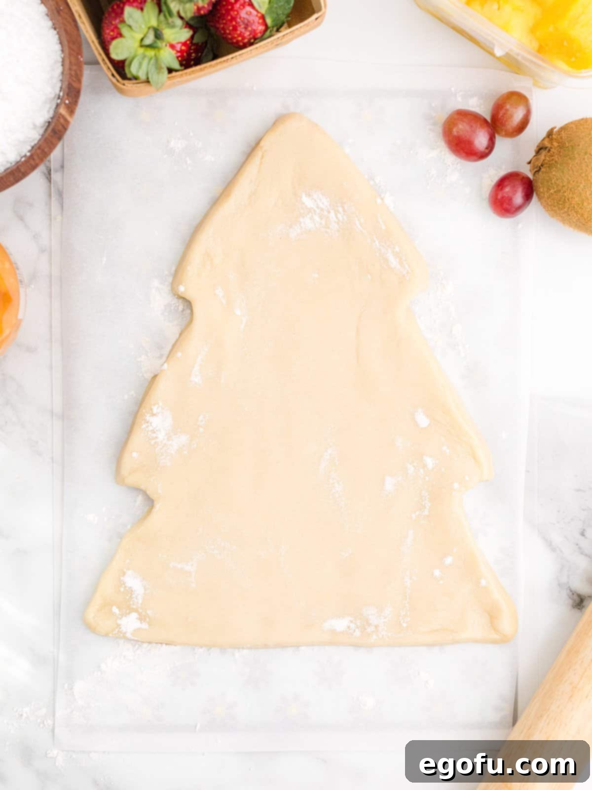Cookie dough meticulously formed into the shape of a Christmas tree on parchment paper, ready for baking.