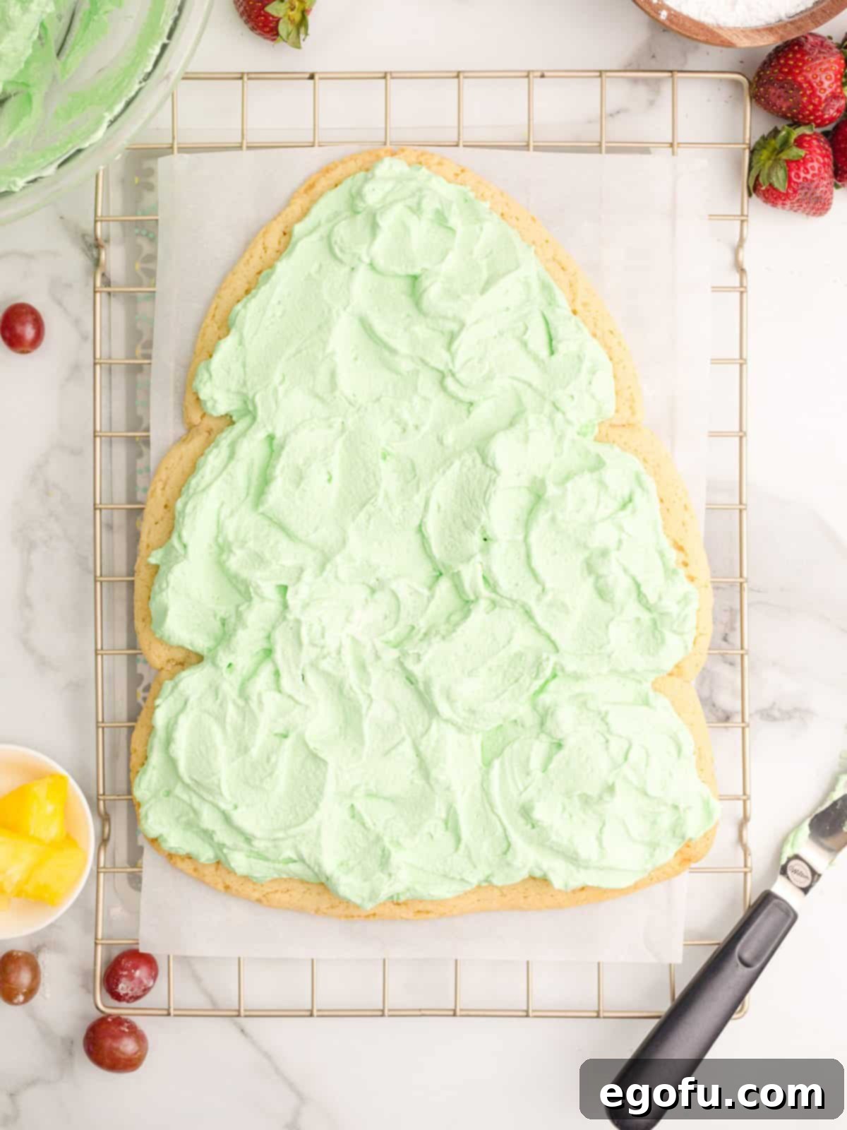 The baked Christmas tree cookie crust generously topped with the green whipped cream, spread smoothly with an offset spatula.