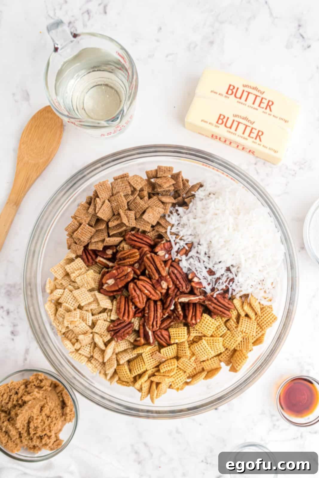 Various dry ingredients, including three types of Chex cereal, coconut, and pecans, mixed in a large bowl.