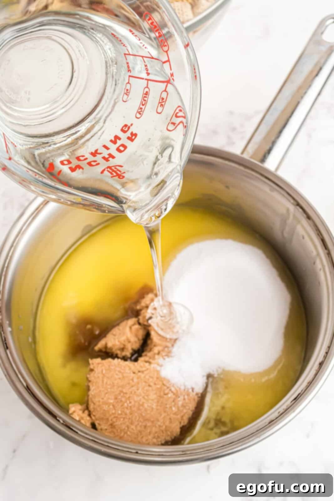 The simmering sweet glaze mixture, including butter, corn syrup, and sugars, in a saucepan.