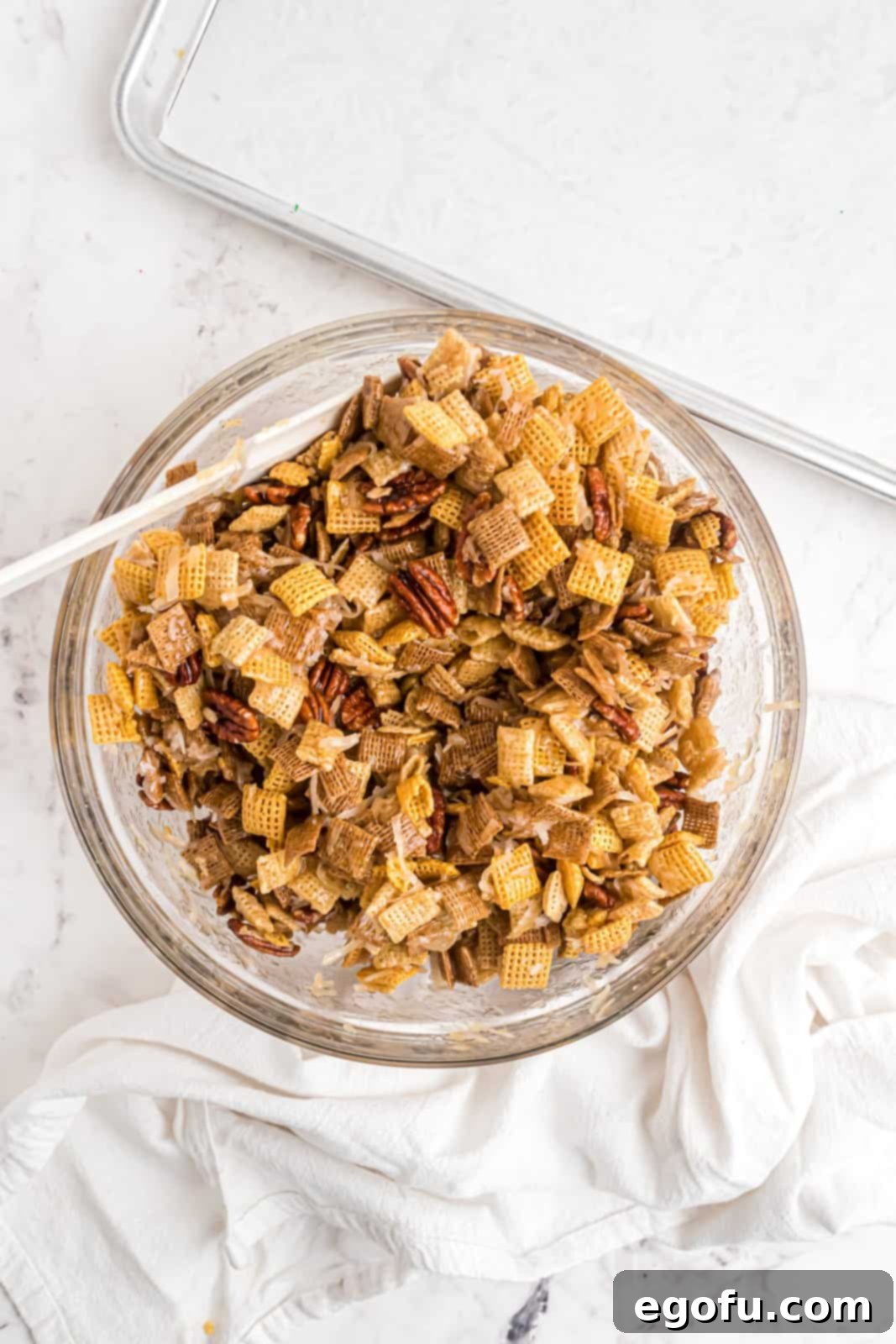 The sweet syrup mixture being poured over the dry Chex cereal and pecans, then stirred to coat.