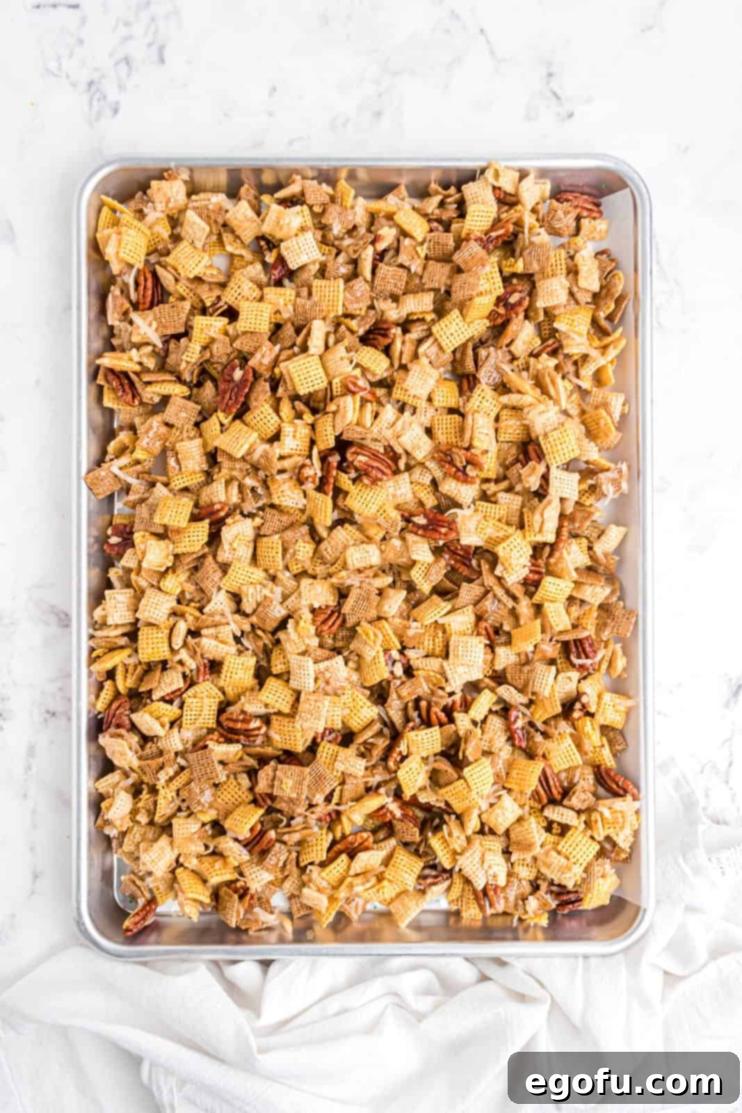 The finished Sweet Holiday Chex Mix spread on a parchment-lined baking pan, cooling and ready to be broken into pieces.