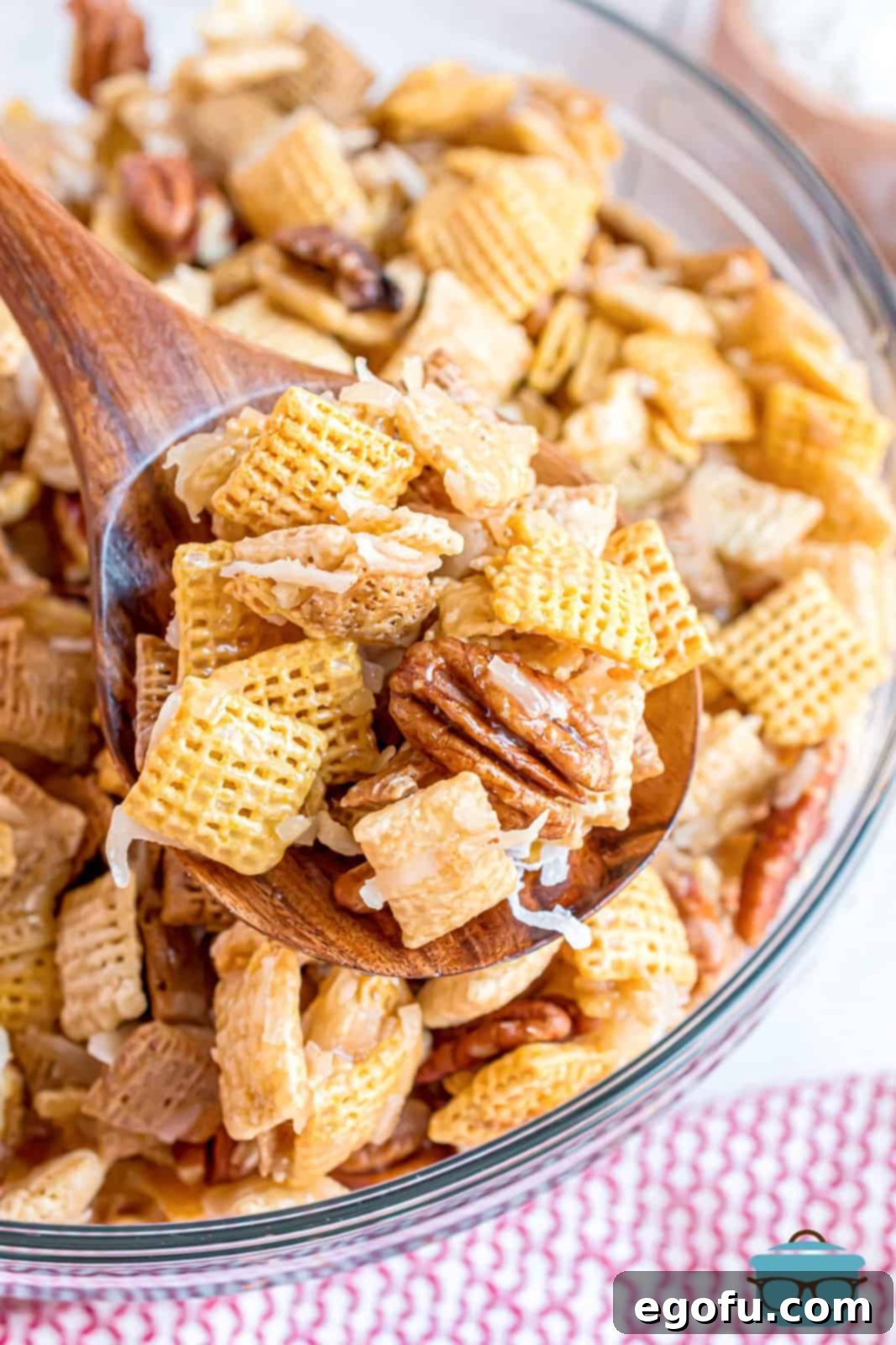 A spoon holding up a delicious cluster of Sweet Holiday Chex Mix from a bowl, showcasing its appeal.